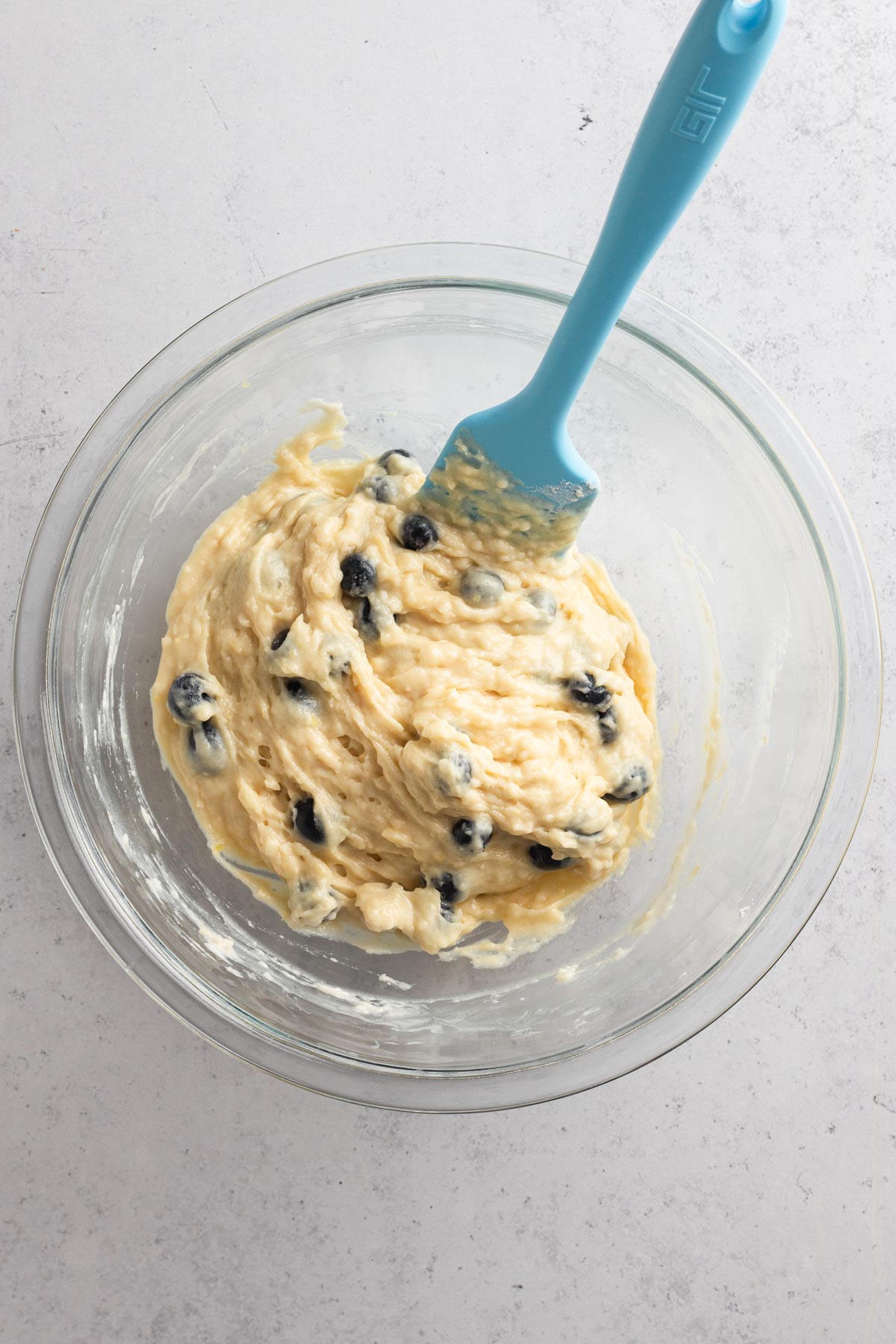 Muffin batter with blueberries in a glass bowl.