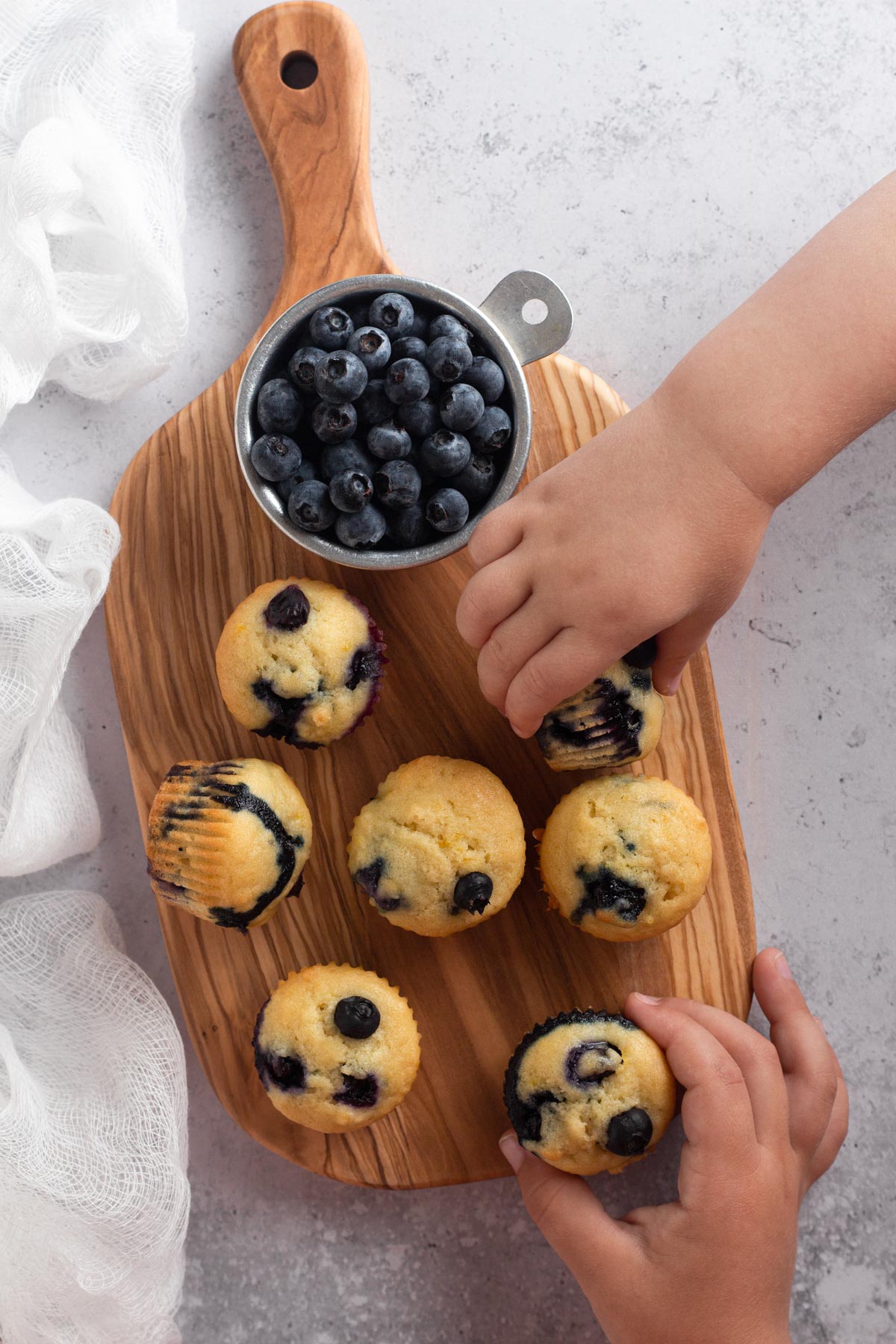 Toddler hands grabbing mini muffins from a wooden cutting board.