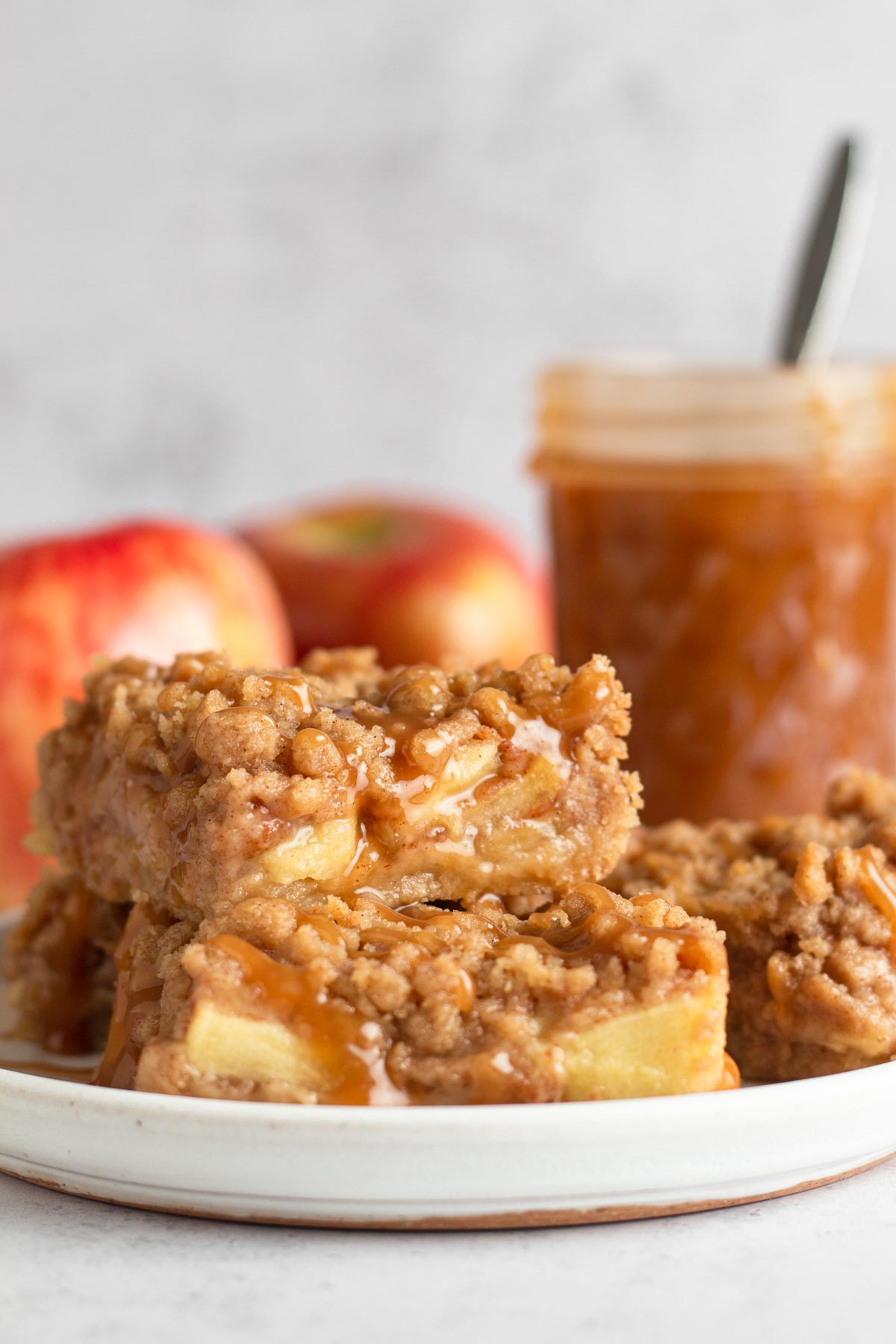 Apple pie bars drizzled with salted caramel sauce stacked on a white plate.