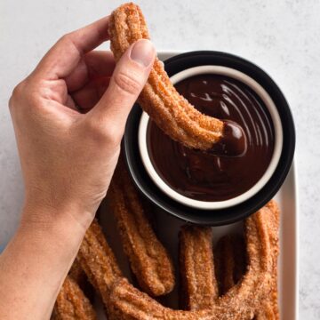 Overhead view of a hand dipping a churro into a bowl of chocolate ganache.