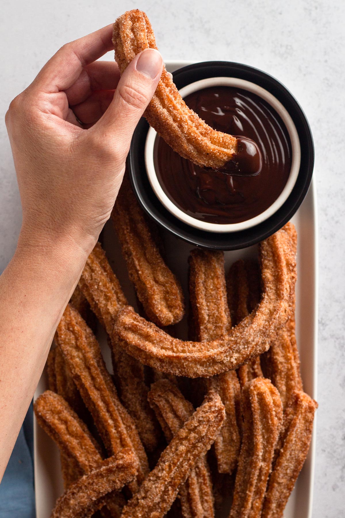 Overhead view of a hand dipping a churro into a bowl of chocolate ganache.