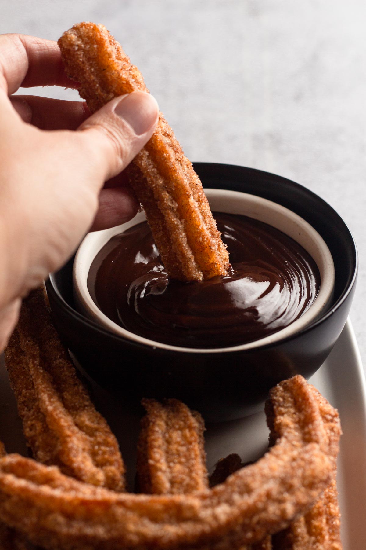Angled view of a hand dipping a churro into a bowl of chocolate ganache.