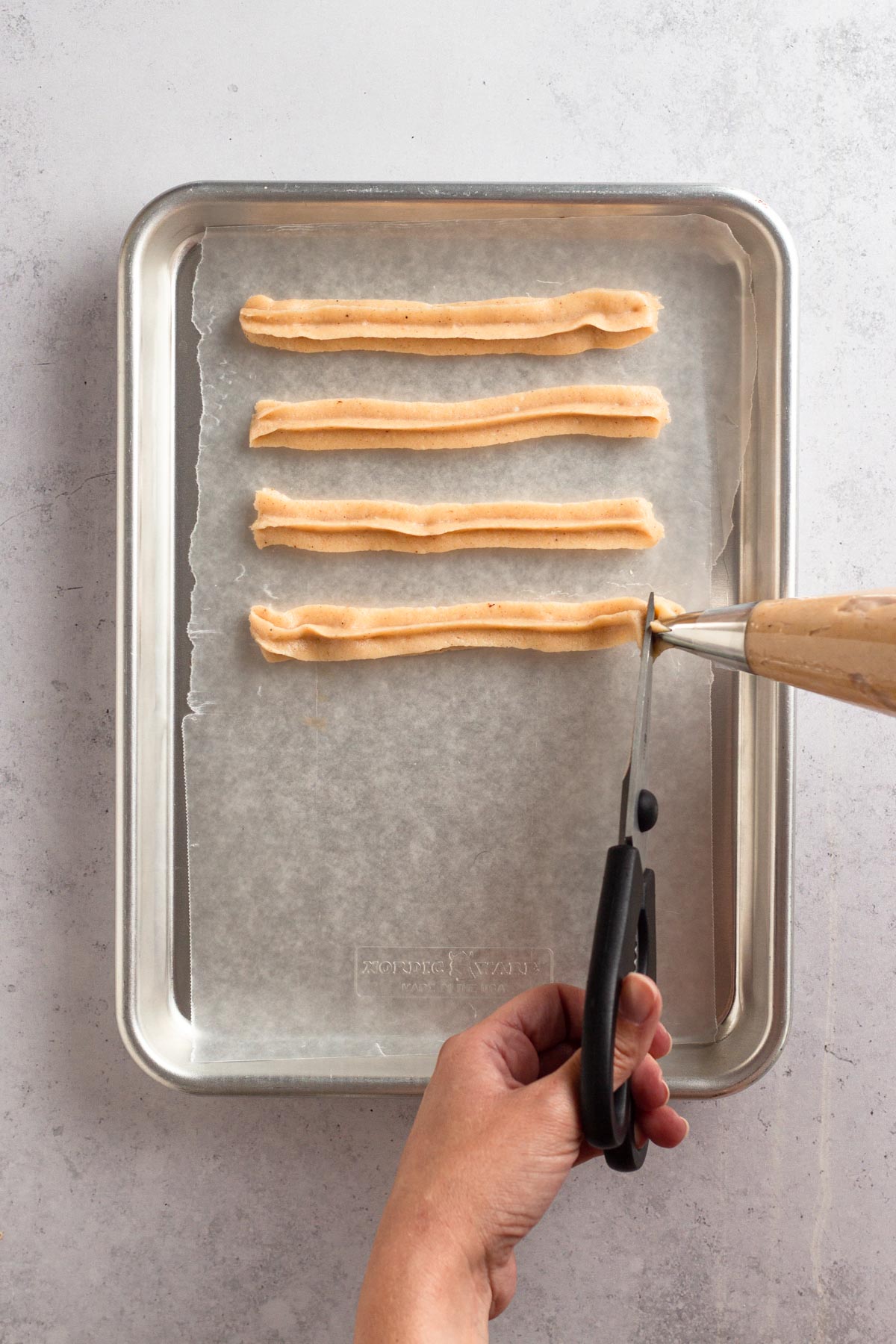 Piping churro dough onto a baking sheet to freeze before frying.