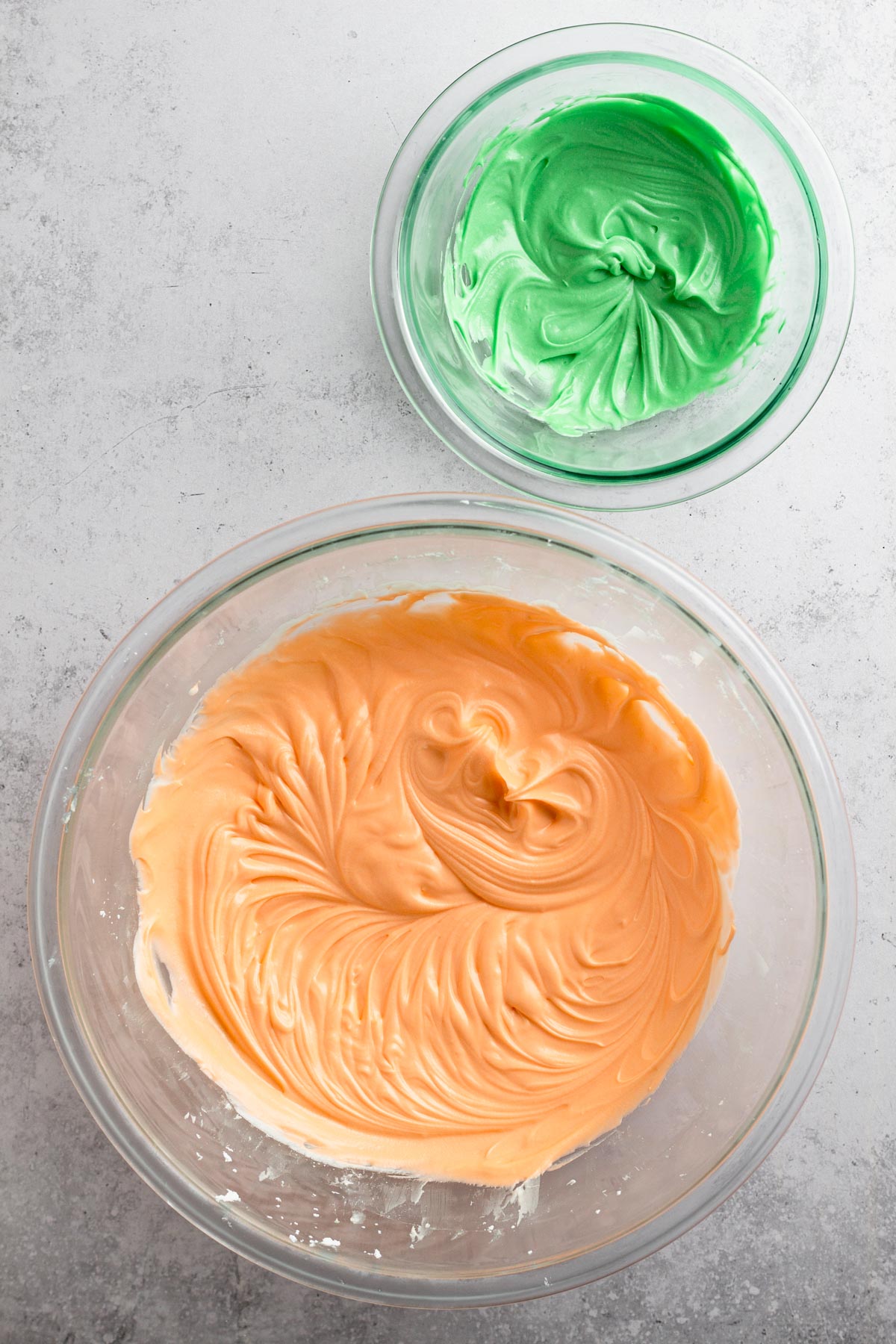 Orange and green frosting in glass bowls.