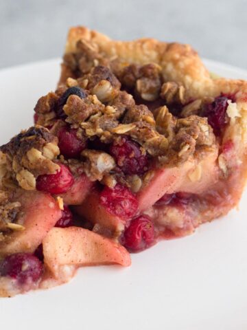 A slice of apple cranberry crumb pie on a white plate.