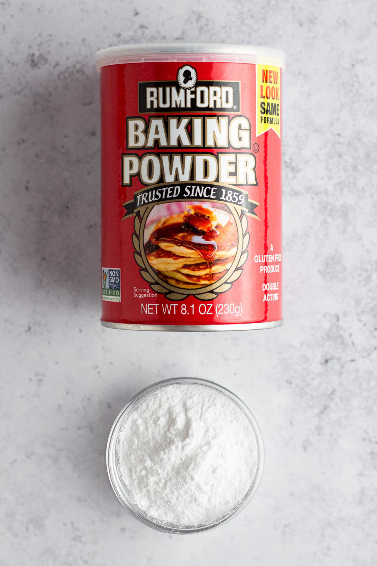 A can of baking powder with a small glass bowl of baking powder.