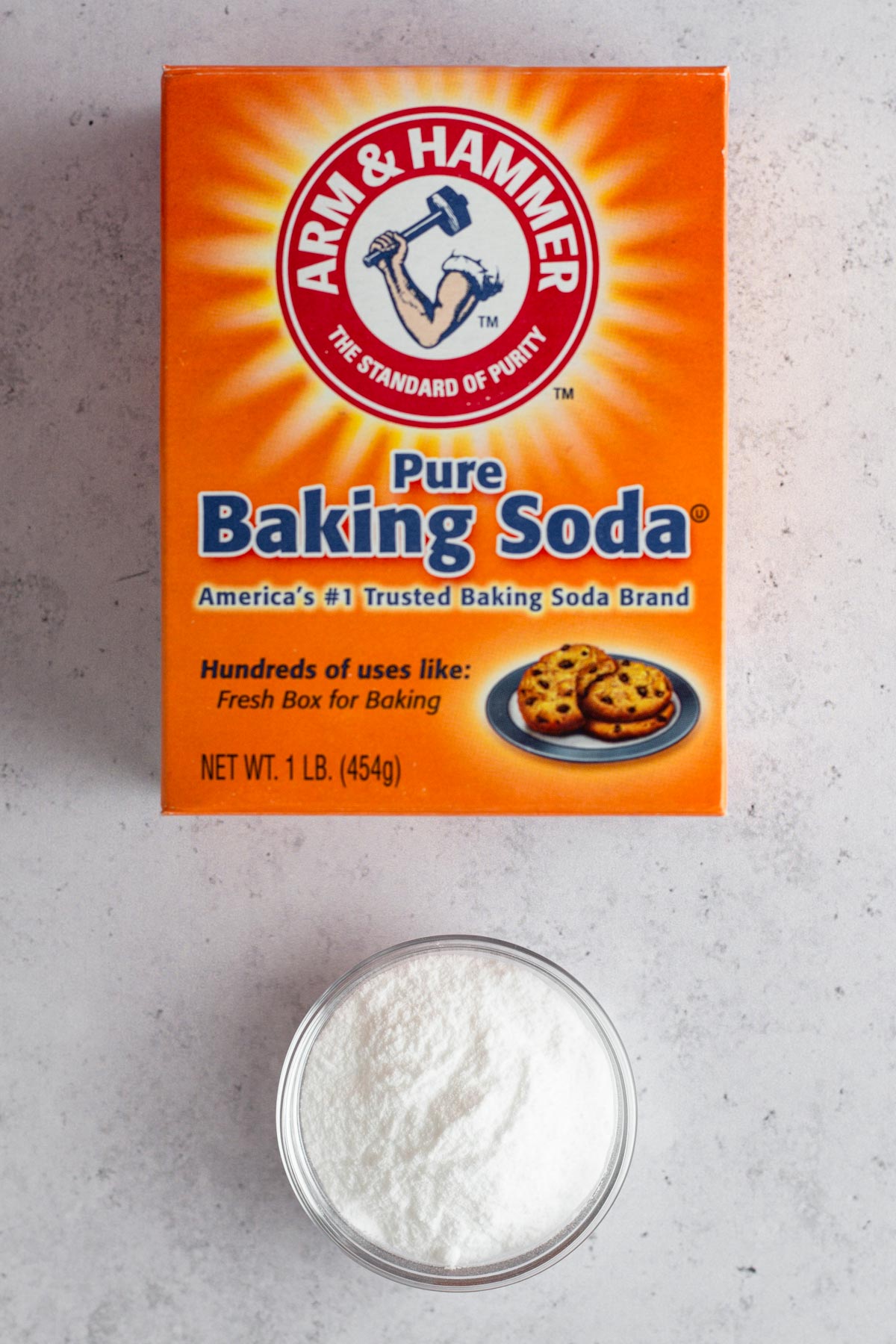 A box of baking soda with a small glass bowl of baking soda.