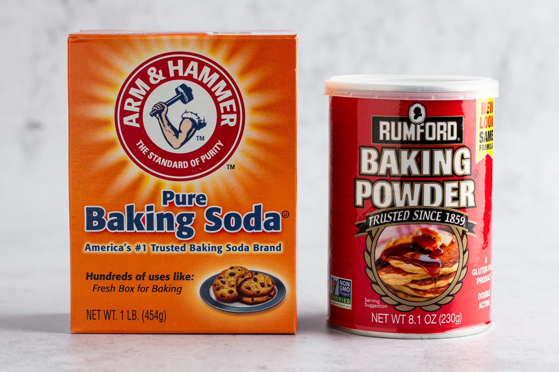 A box of baking soda and a can of baking powder on a gray surface.