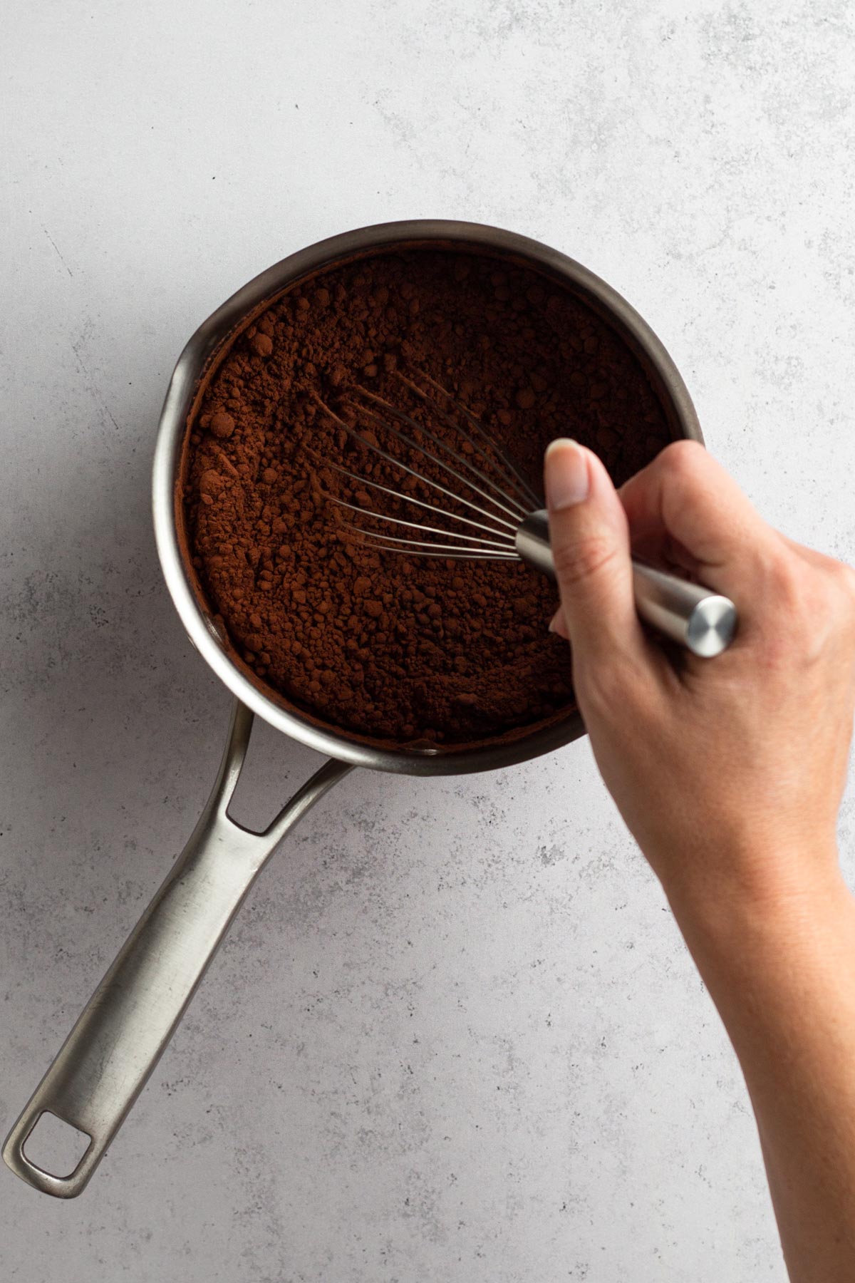 Milk, sugar, and cocoa being whisked together in a saucepan.