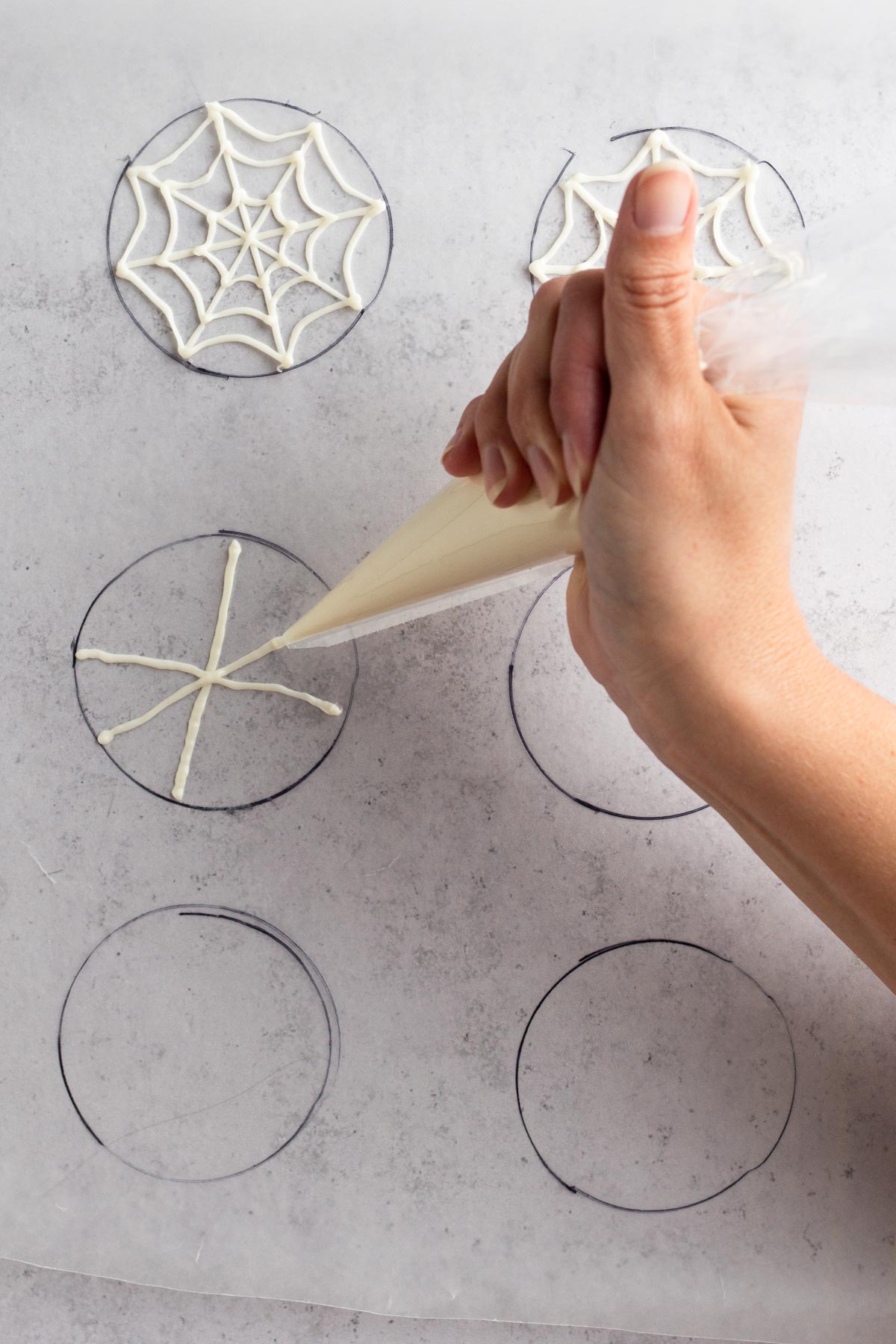Hand piping intersecting lines of melted white chocolate onto wax paper.