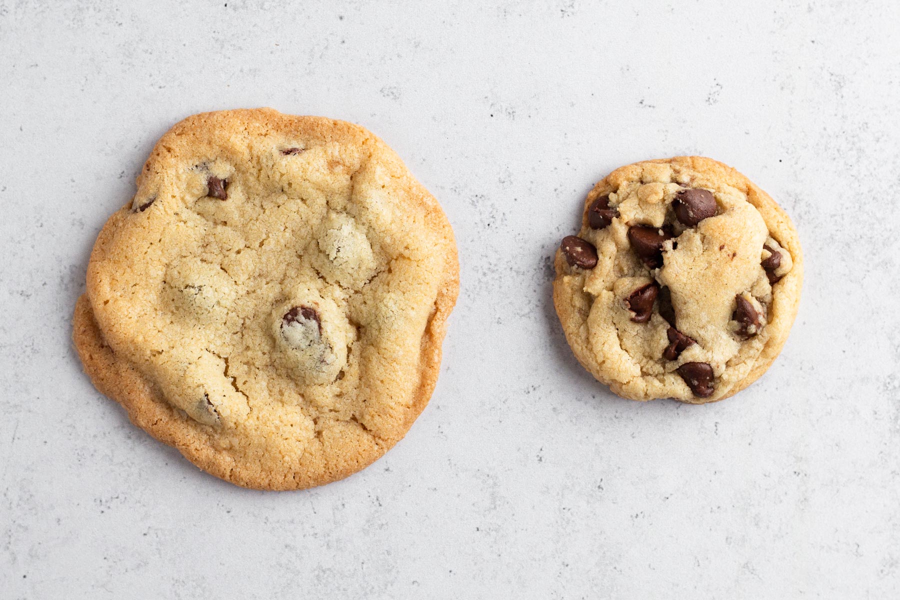 Flat and thick chocolate chip cookies side by side on a gray surface.