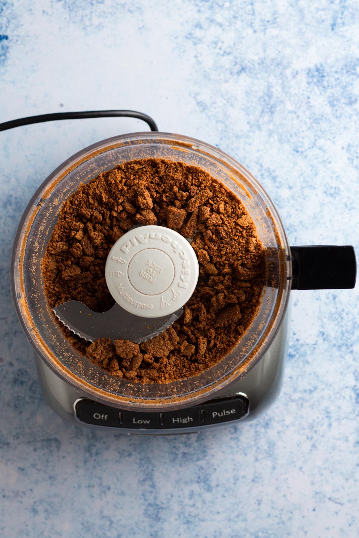 Gingersnap cookie crumbs in the bowl of a food processor.
