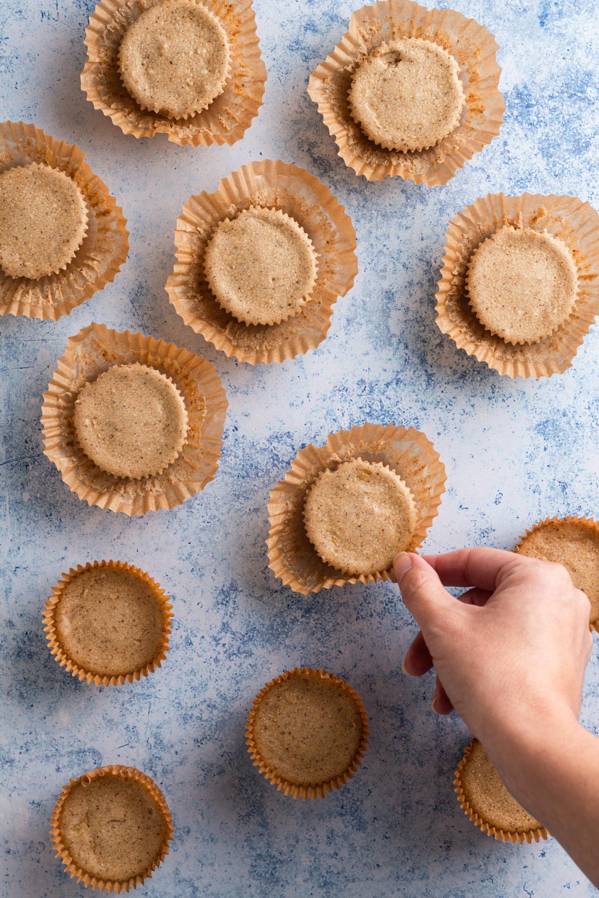 Hand removing muffin liners from chilled cheesecakes.