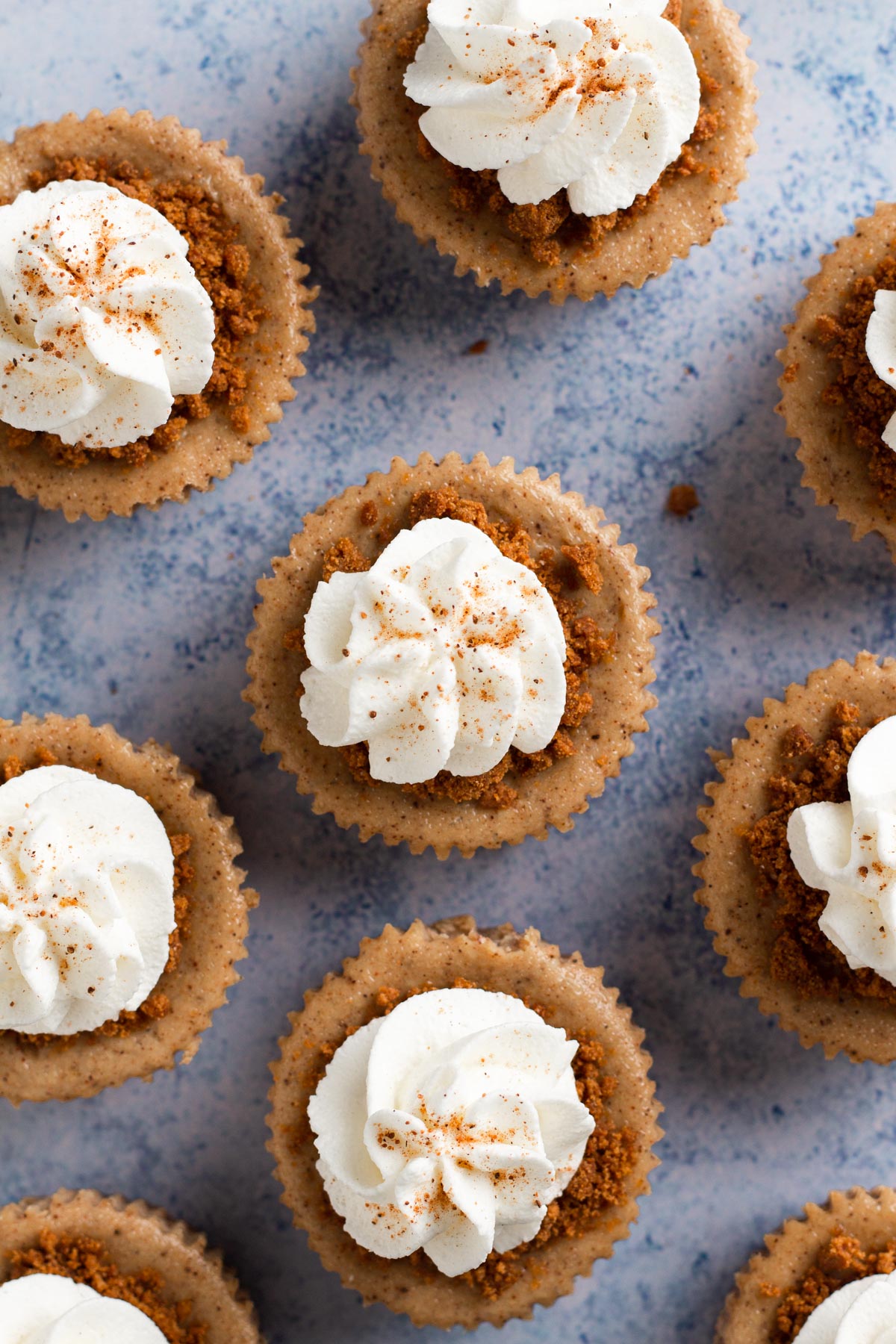 Individual cheesecakes topped with swirls of whipped cream and a dusting of ground nutmeg.