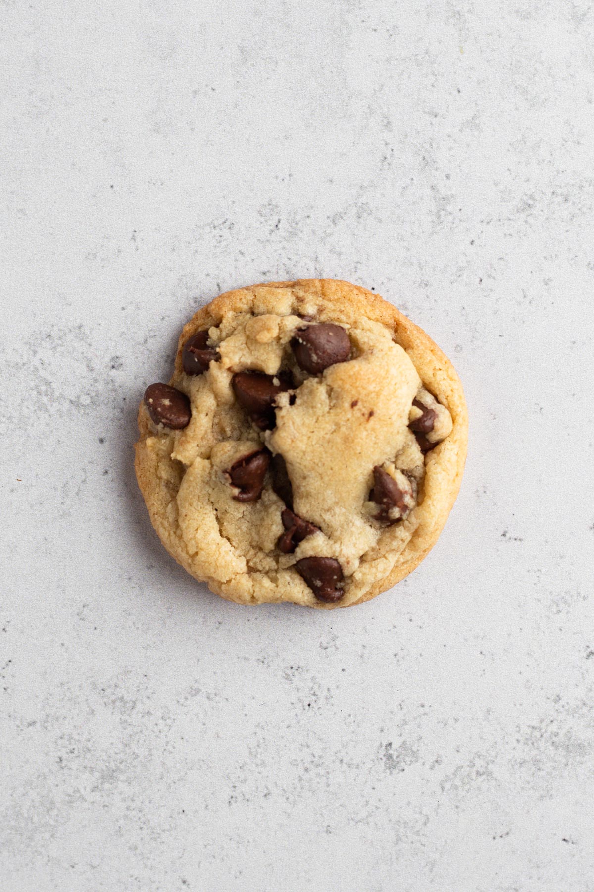 A thick chocolate chip cookie on a gray surface.