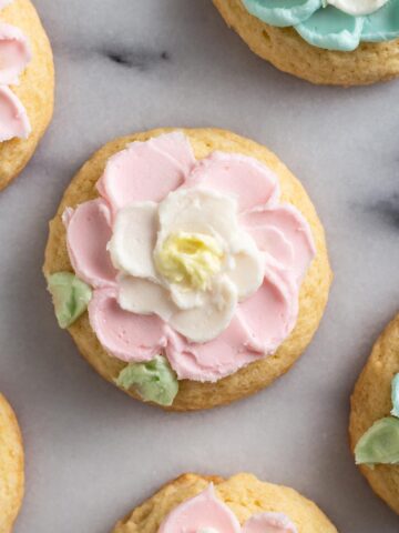 Overhead view of sugar cookies with buttercream frosting flowers on a marble surface.