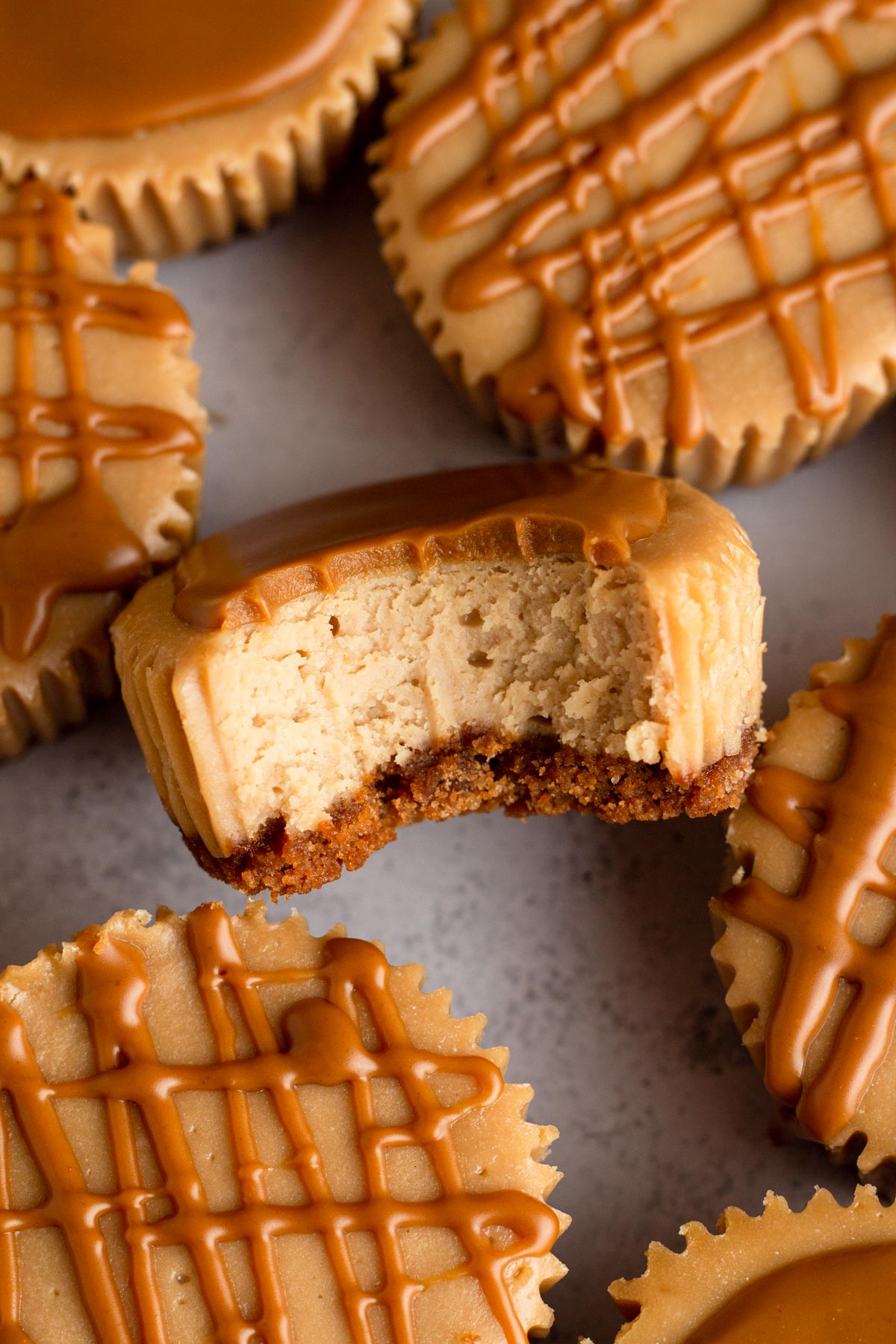 A bitten mini Biscoff cheesecake surrounded by more mini cheesecakes drizzled with cookie butter.