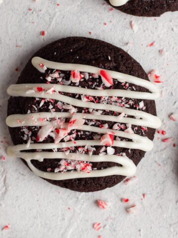 Overhead view of chocolate cookies with white chocolate and crushed candy canes on a white surface.