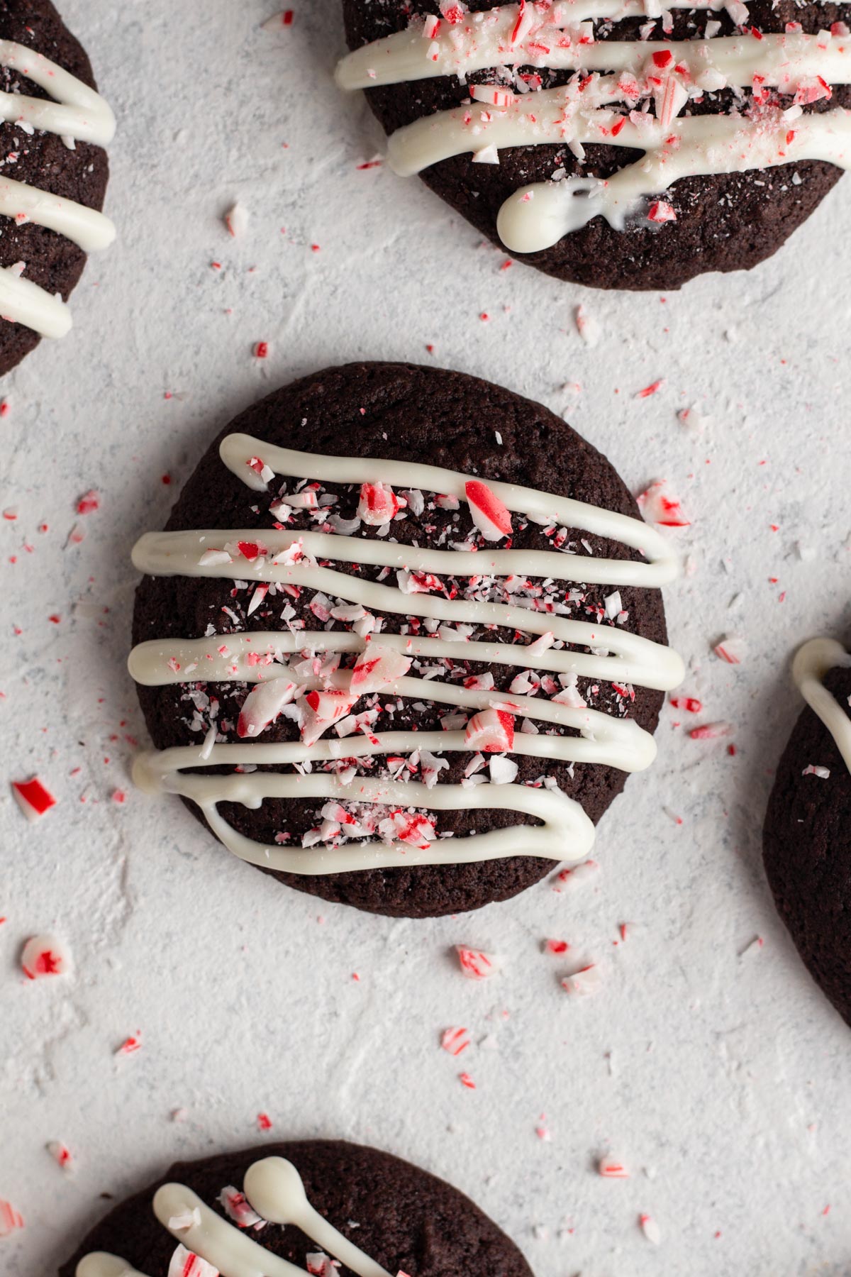 Overhead view of chocolate cookies with white chocolate and crushed candy canes on a white surface.