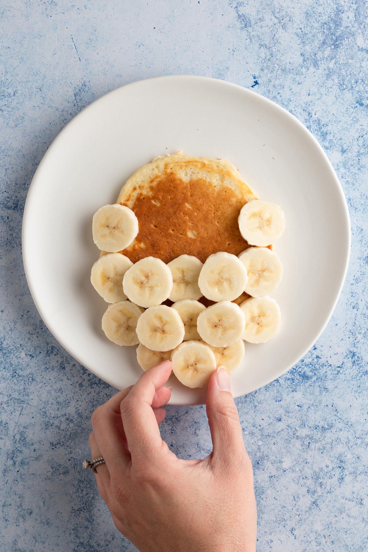 Hand placing slices of banana in a triangle shape below the pancake.
