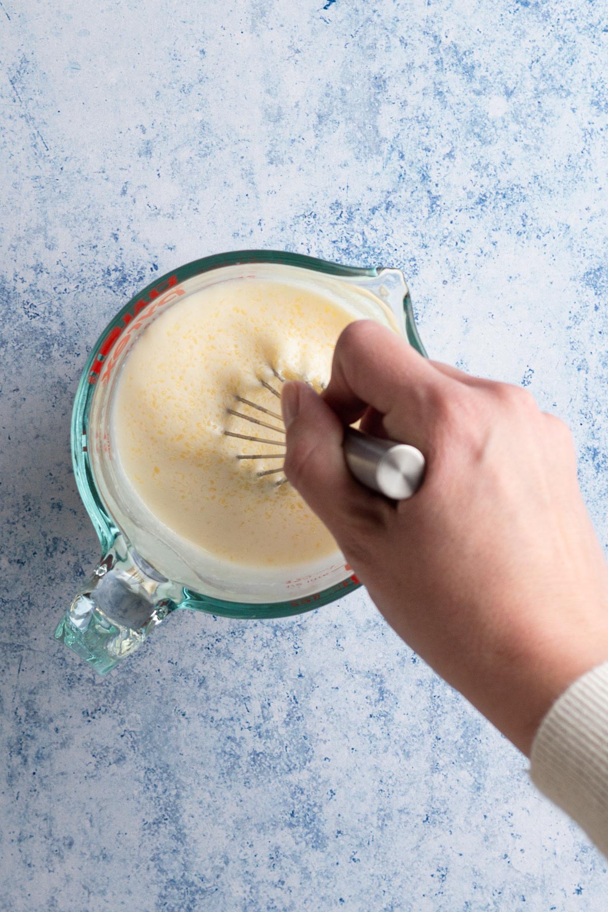 Hand whisking wet ingredients together in a glass measuring cup.