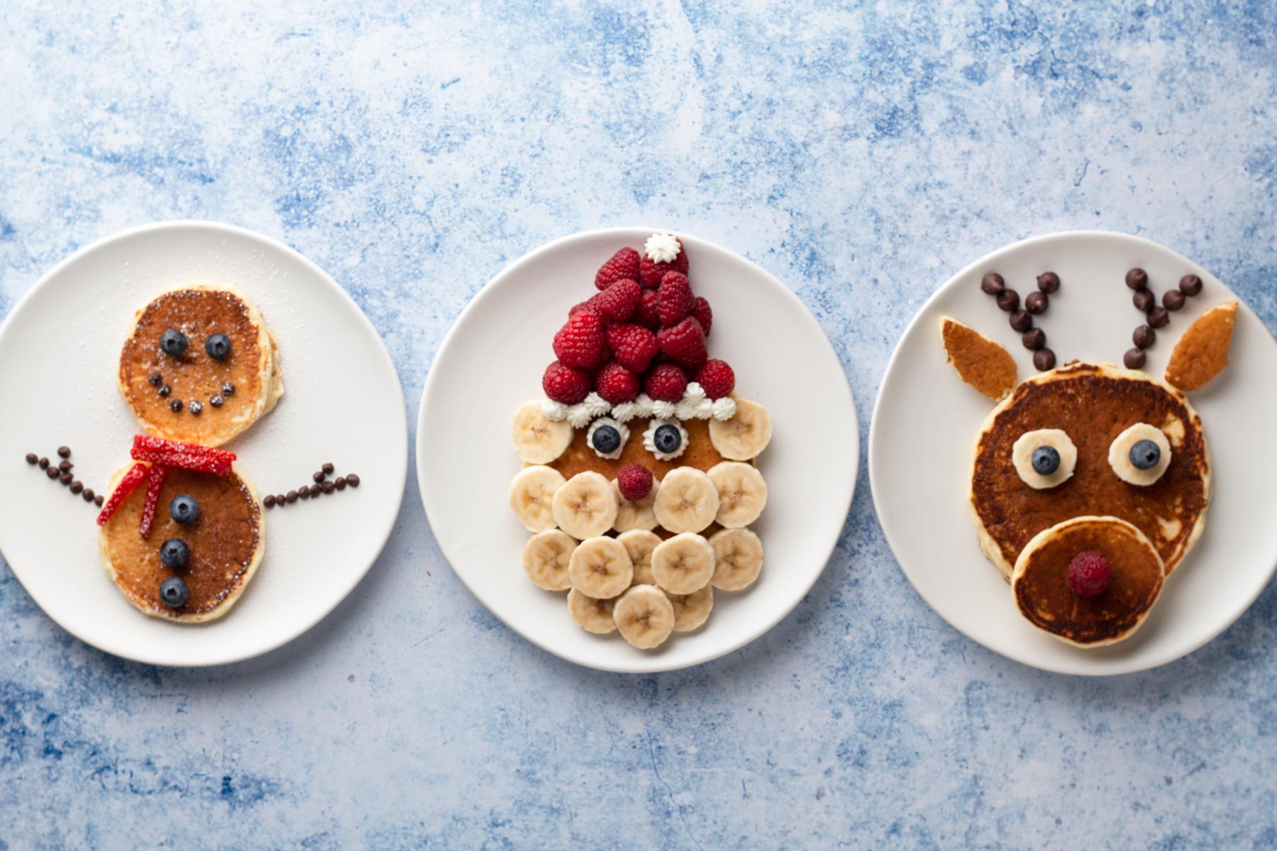 Pancakes on white plates decorated like a snowman, Santa, and a reindeer.