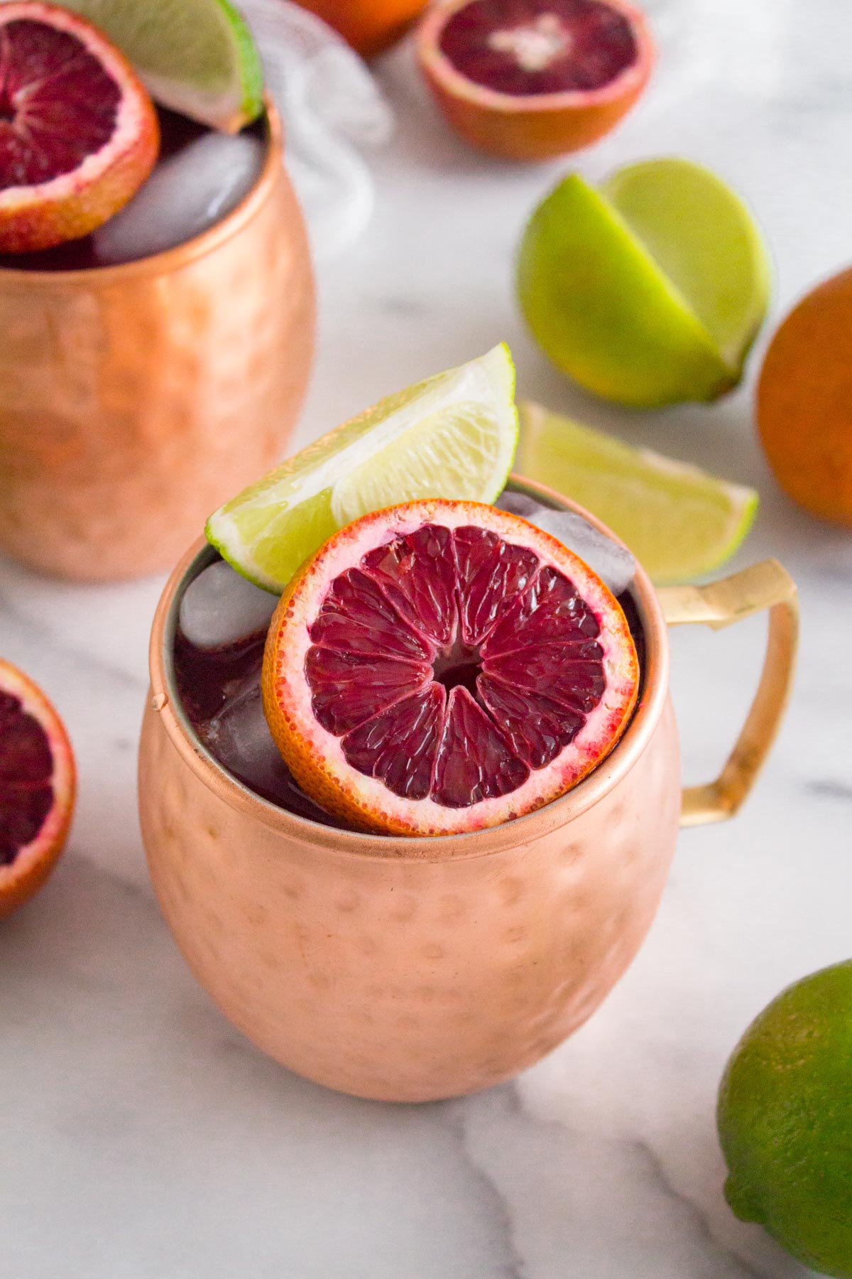 Cocktail garnished with fresh blood orange and lime slices in a copper Moscow mule mug.