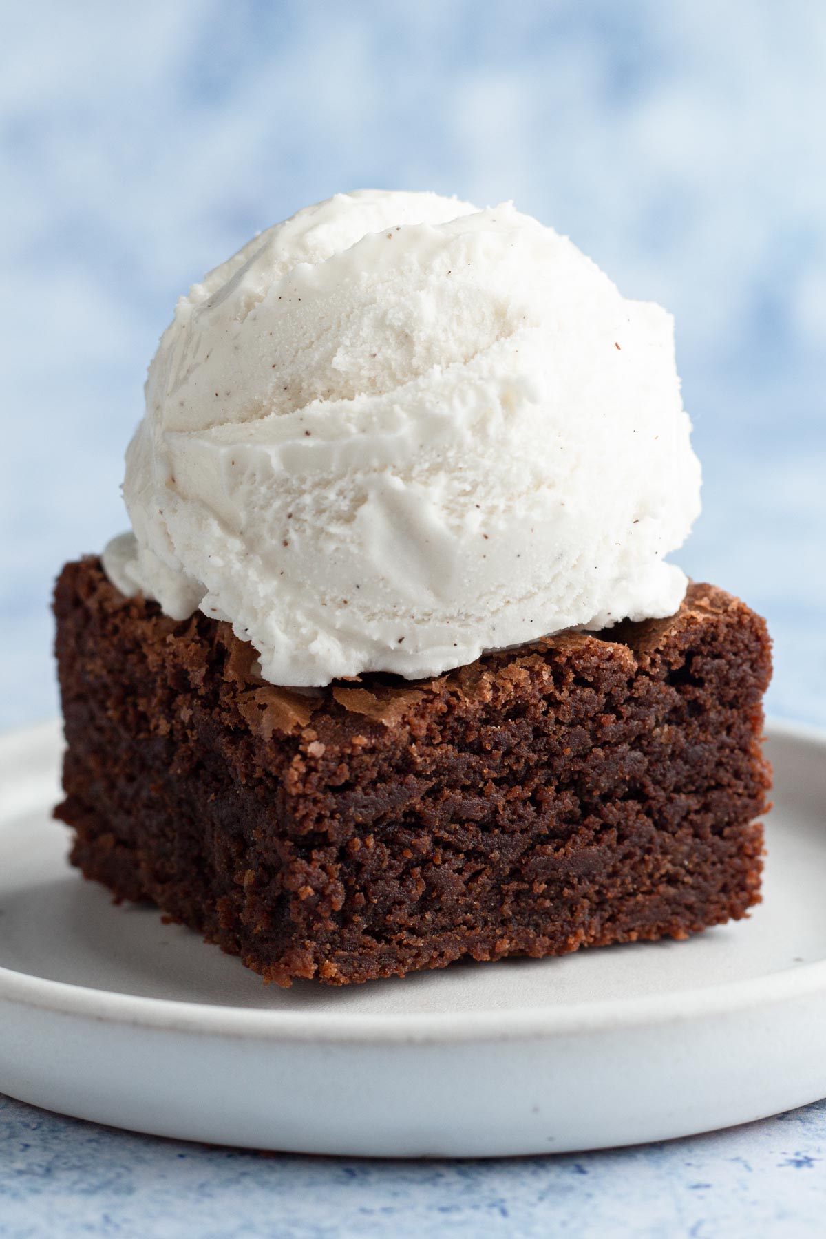 Brownie on a white plate with a scoop of vanilla ice cream.