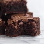 Side view of a bitten brownie stacked on a white marble surface.