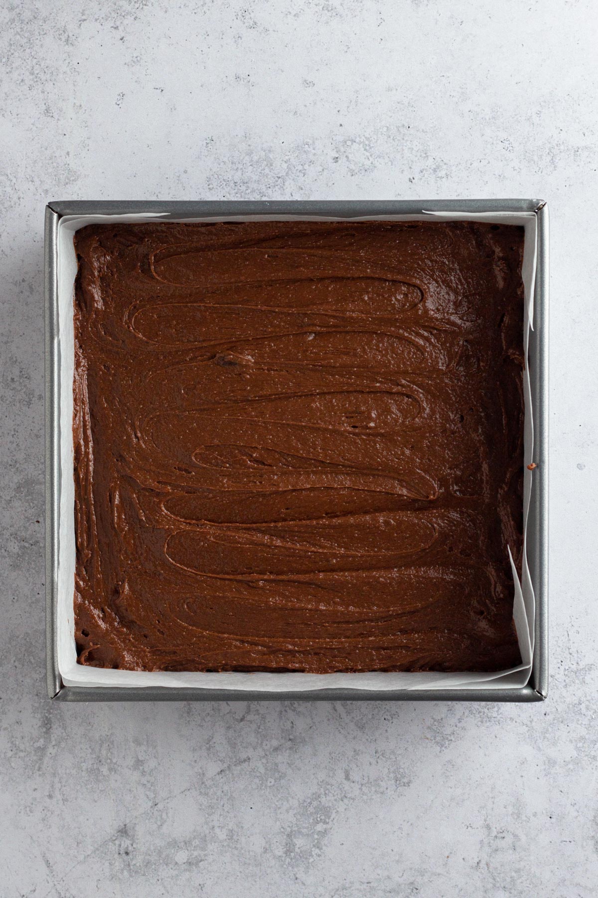 Brownie batter in a square metal pan lined with parchment paper.