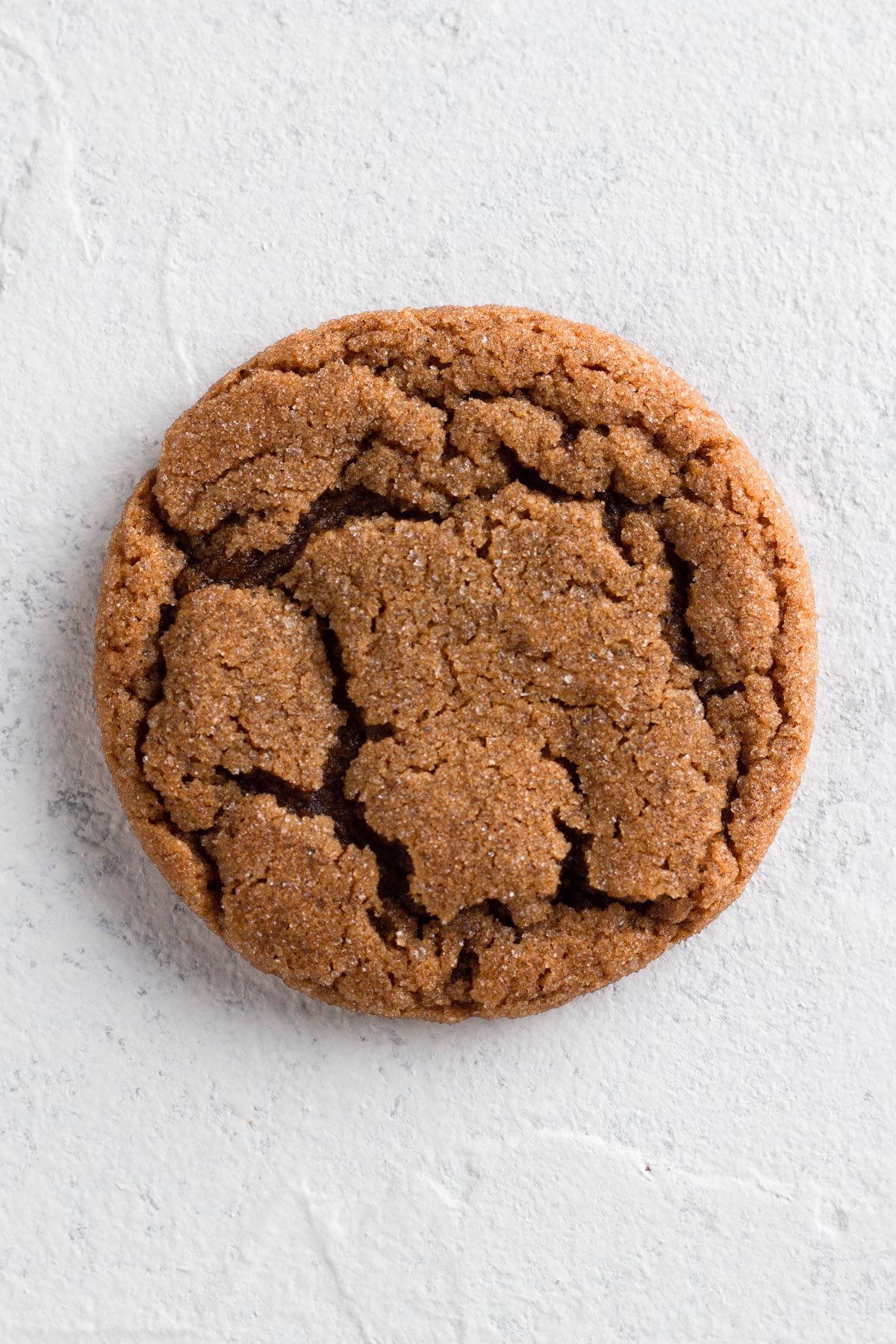 Close up overhead view of a molasses crinkle cookie on a white textured surface.