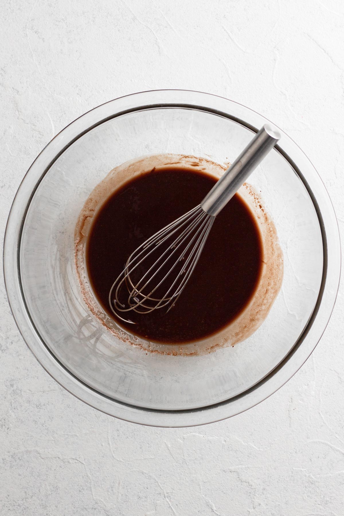 Melted butter and chocolate in a glass mixing bowl with a metal whisk.