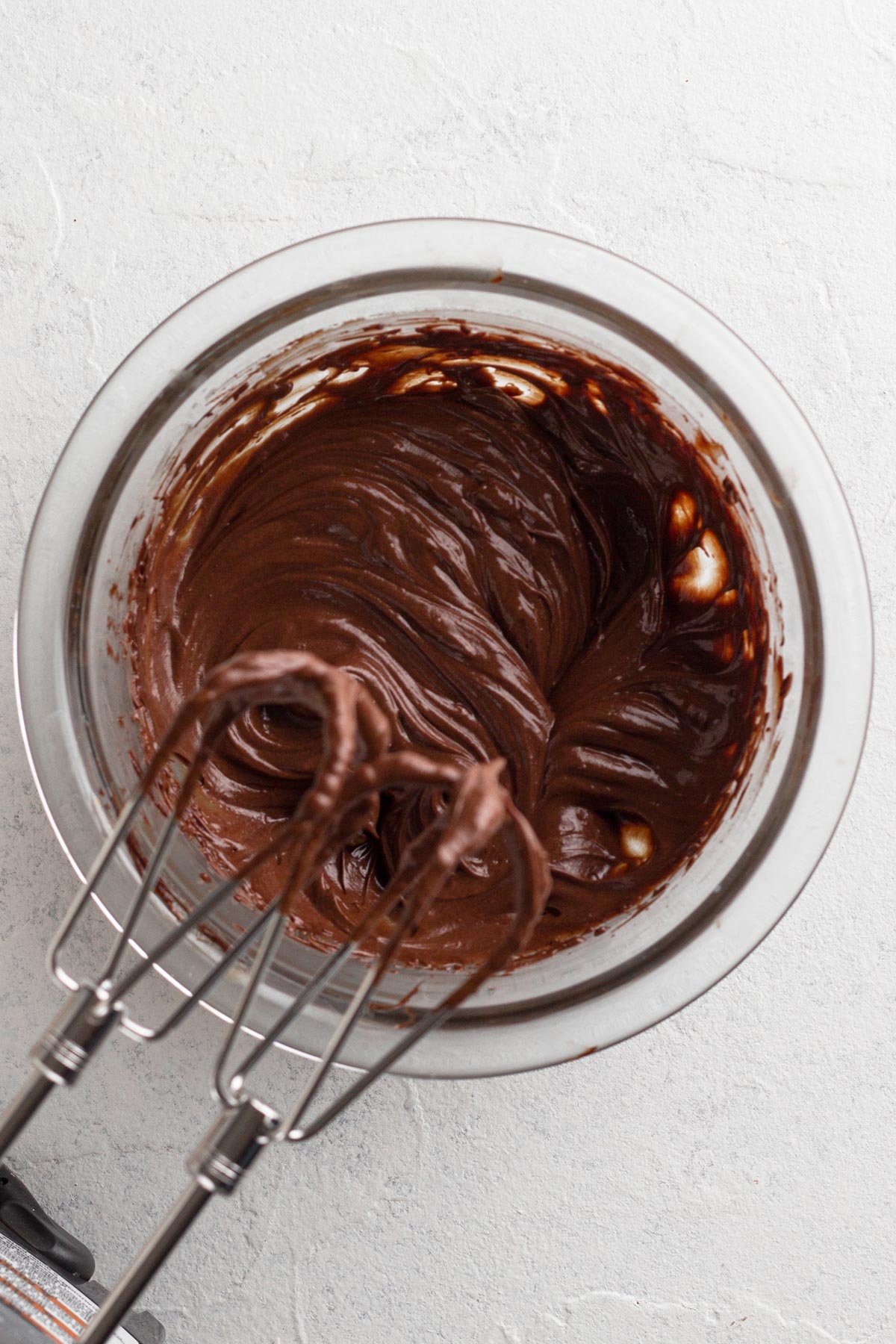 Whipped chocolate ganache in a glass mixing bowl with an electric hand mixer.