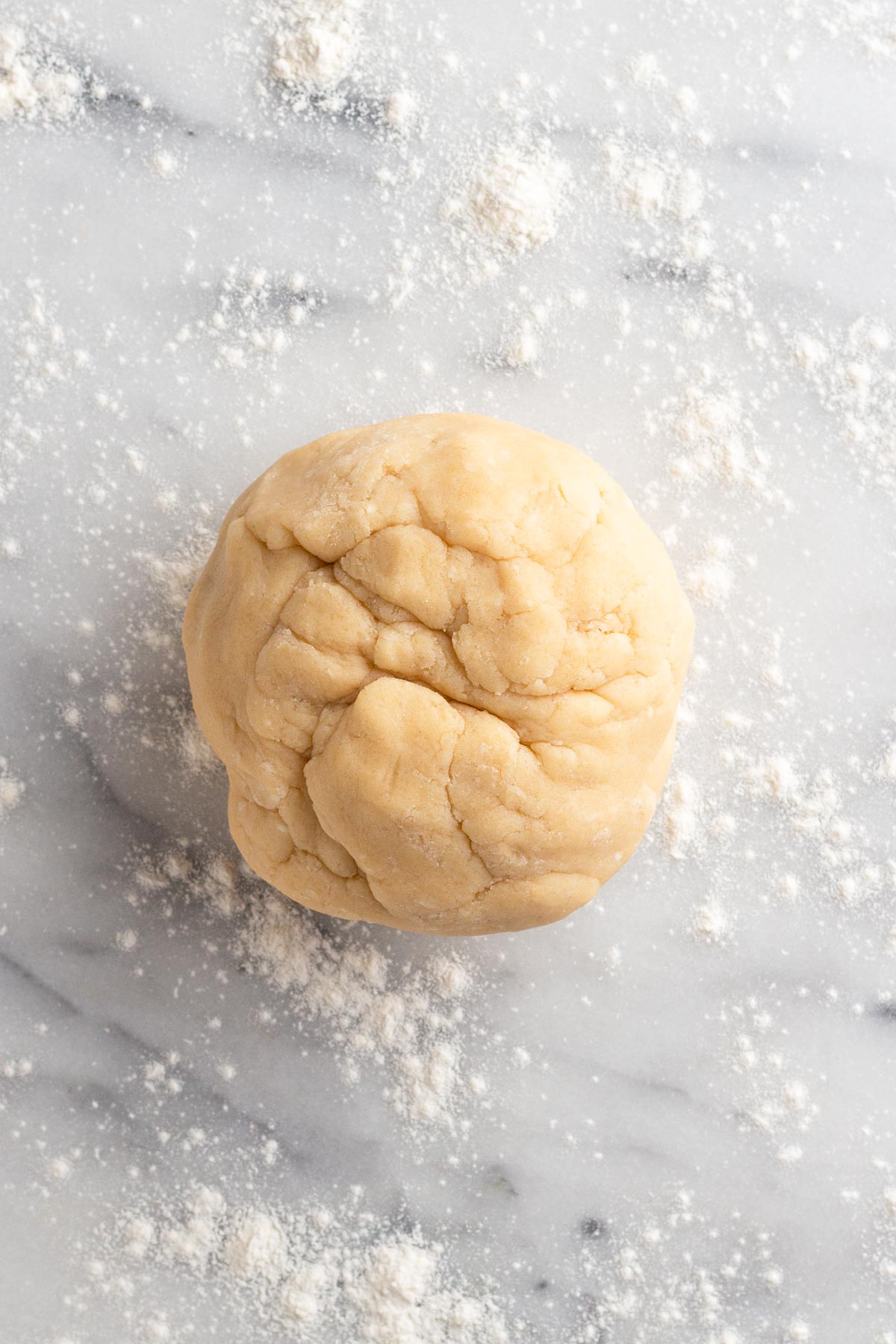 Ball of cookie dough on a floured marble surface.