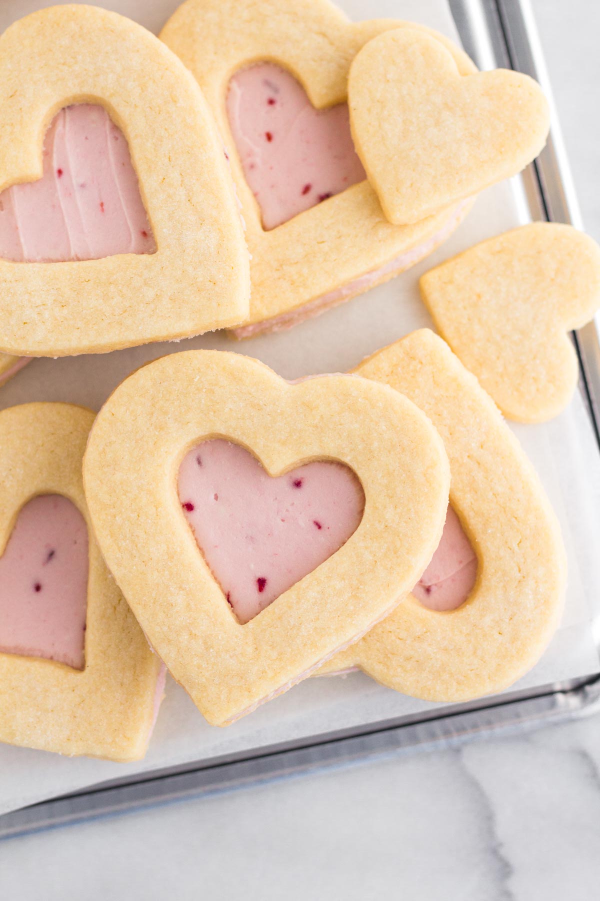 Close up view of heart sugar cookies with raspberry buttercream frosting stacked on a baking sheet.