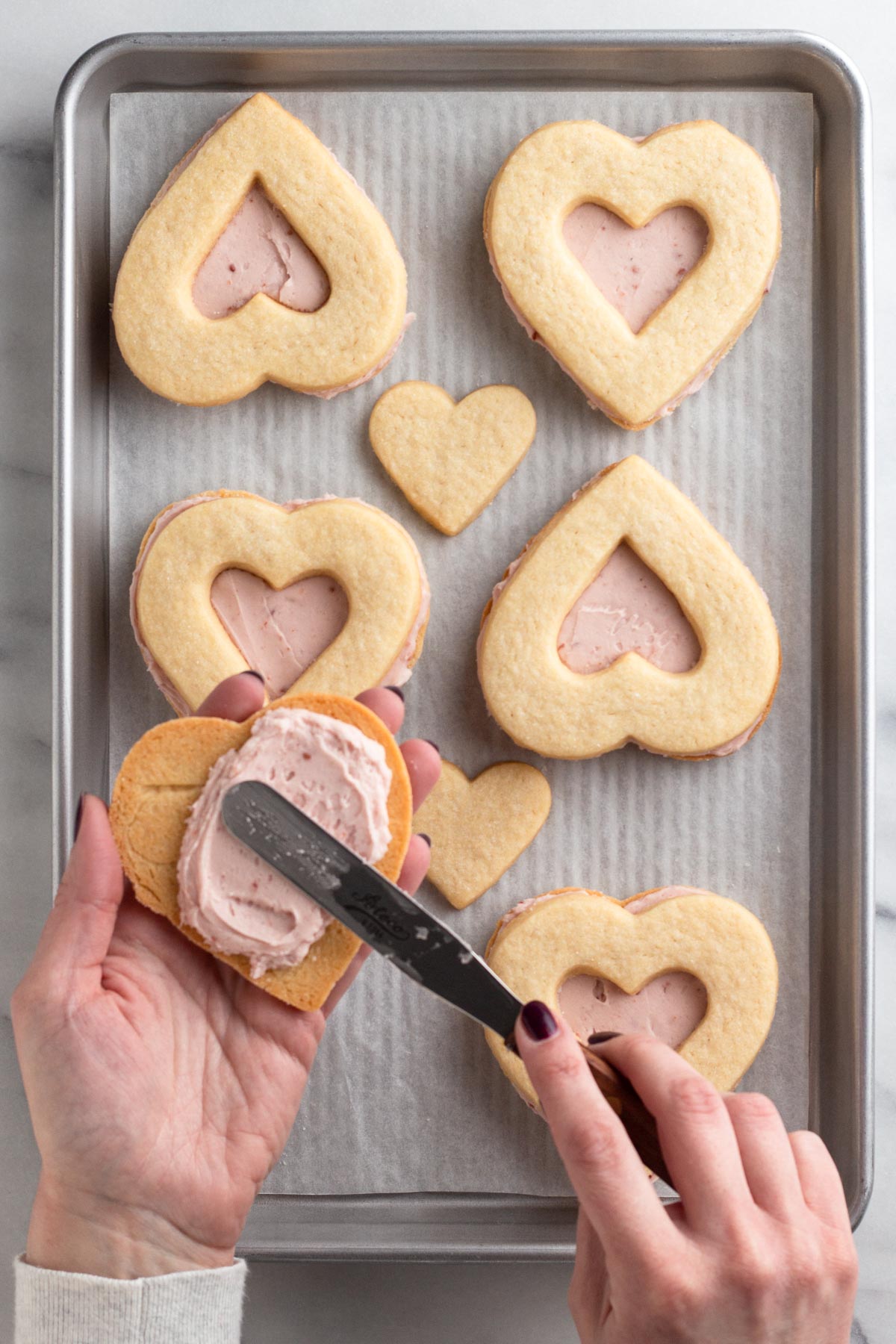 Hands holding sugar cookie and spreading frosting onto the cookie using an icing spatula.