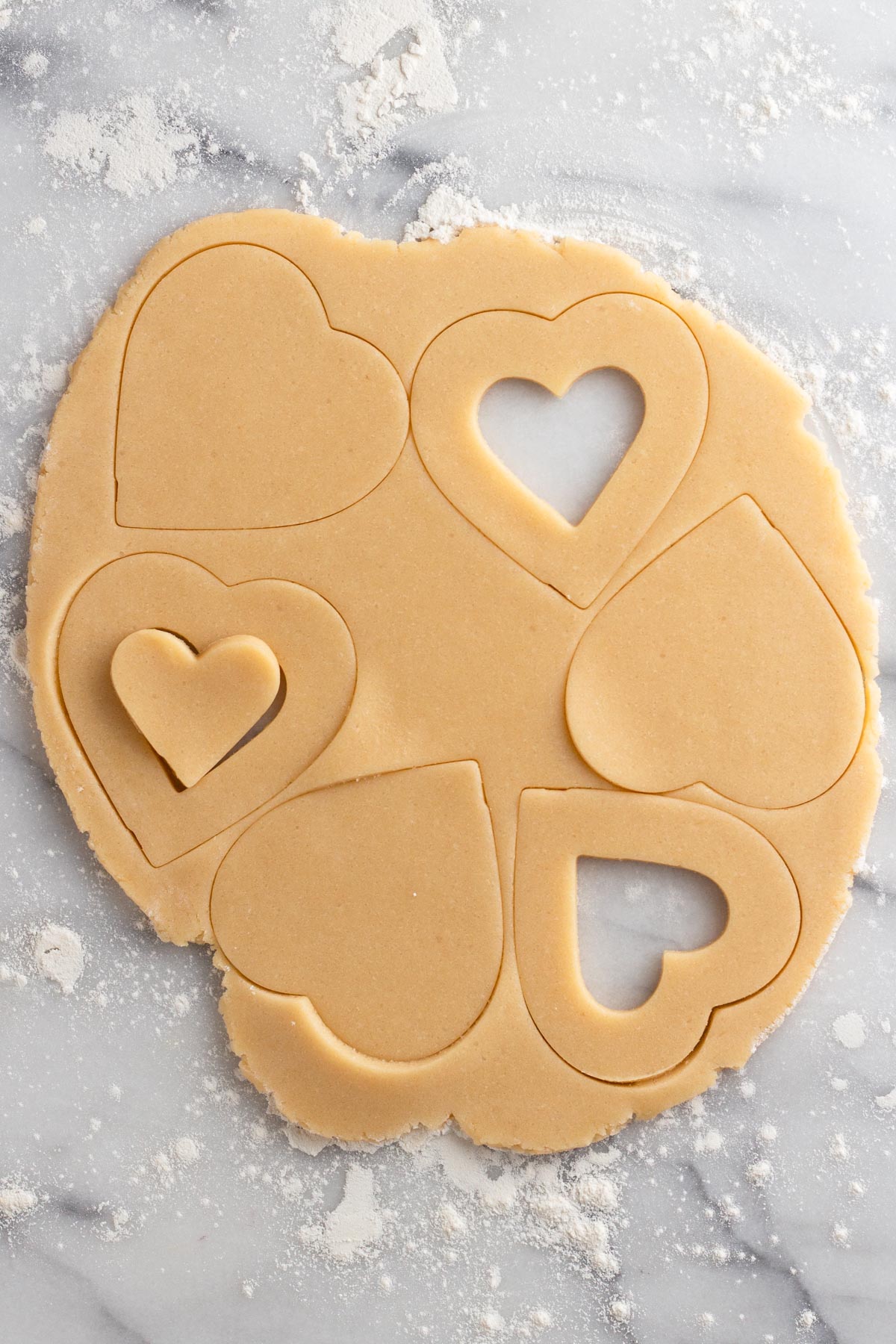 Rolled out cookie dough on a marble surface with heart shapes cut out.