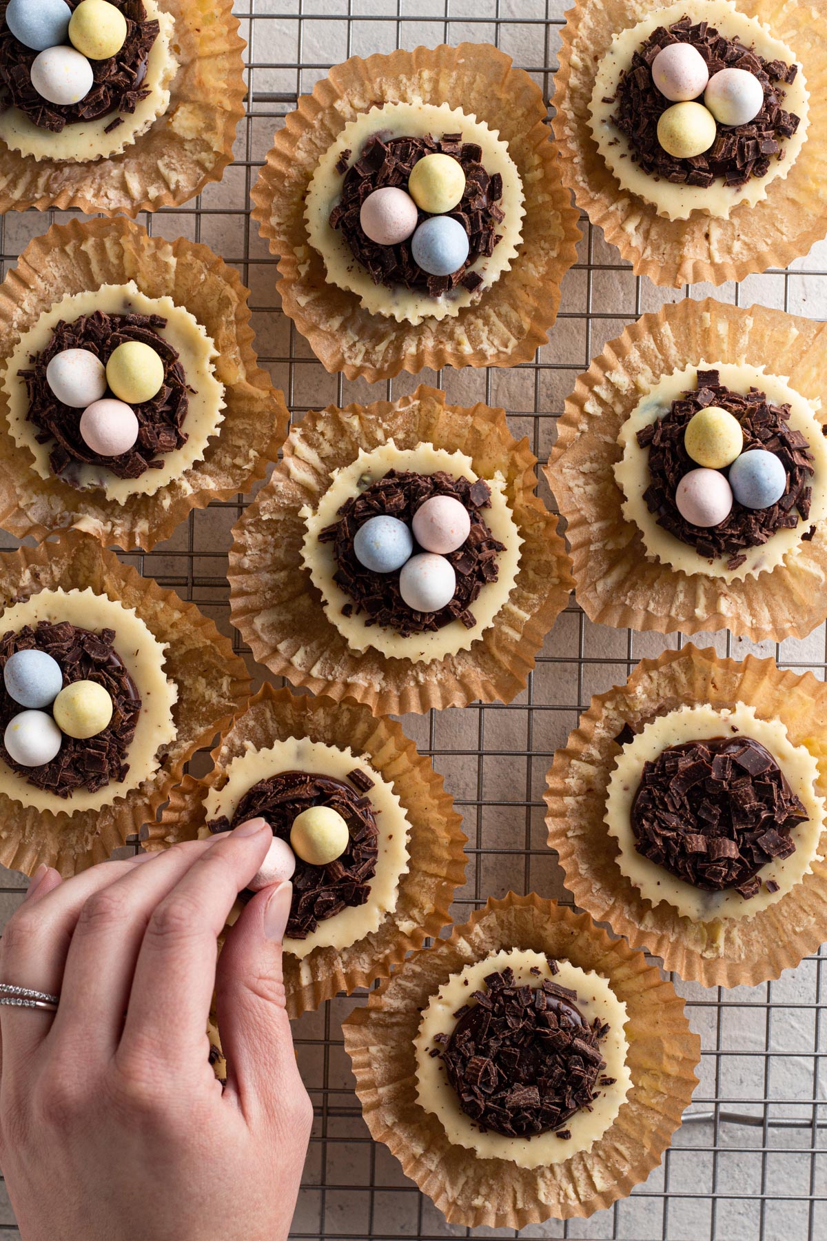 Hand placing mini eggs into "nests" on tops of cheesecakes.