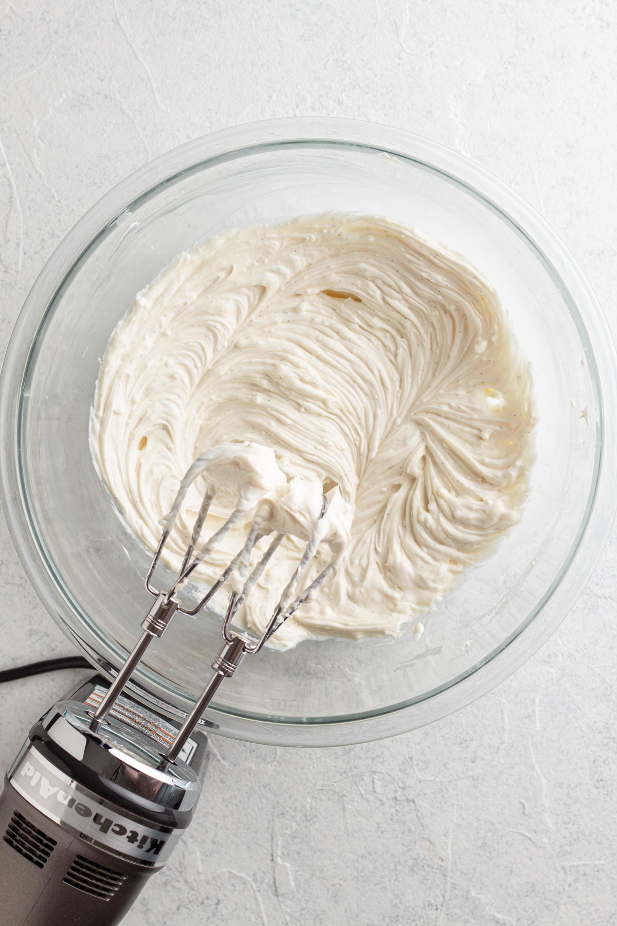 Cream cheese and other ingredients blended together in a glass mixing bowl.