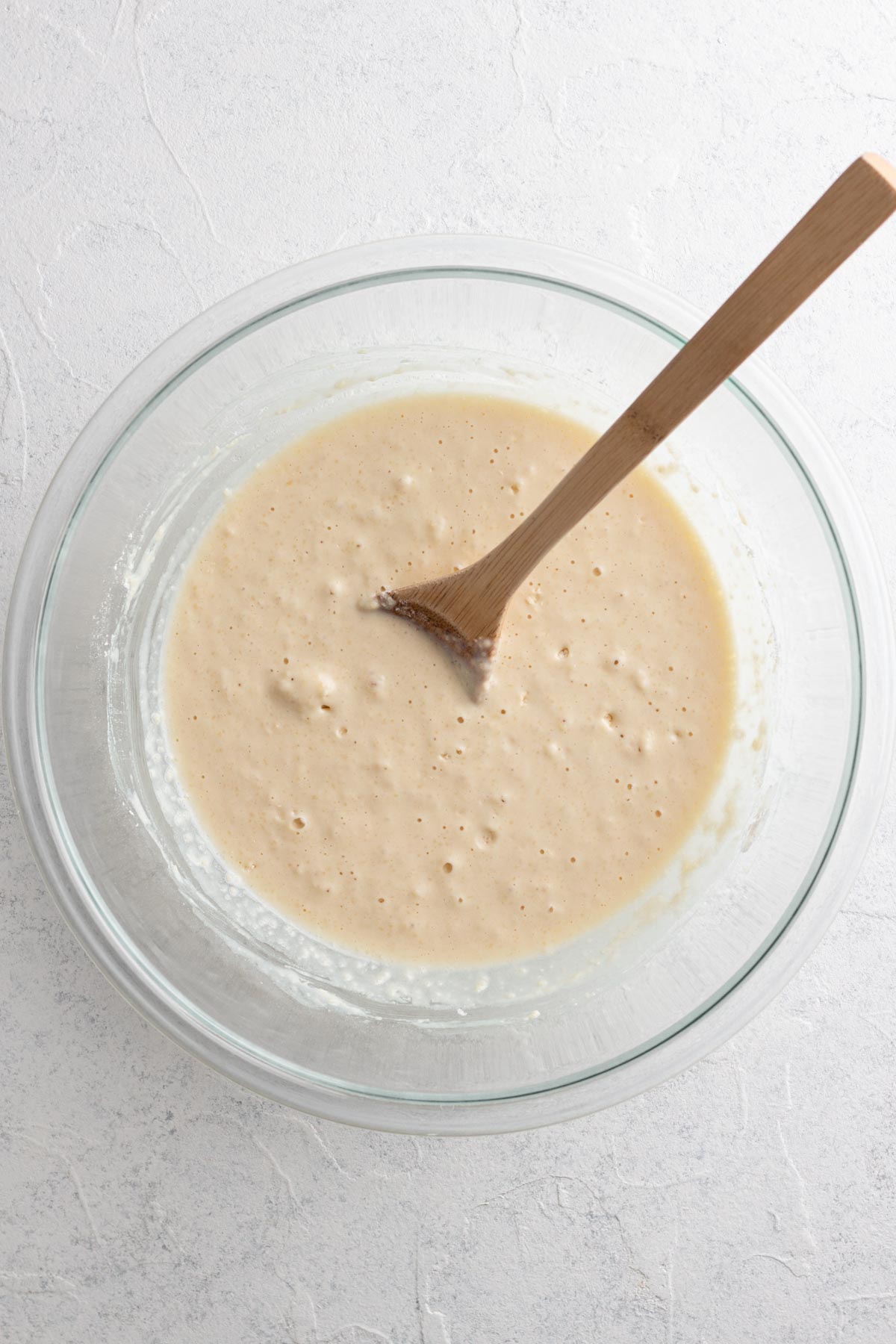 Pancake batter in a glass mixing bowl with a wooden spoon.