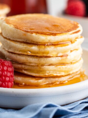 Pancakes stacked on a white plate with drips of maple syrup.