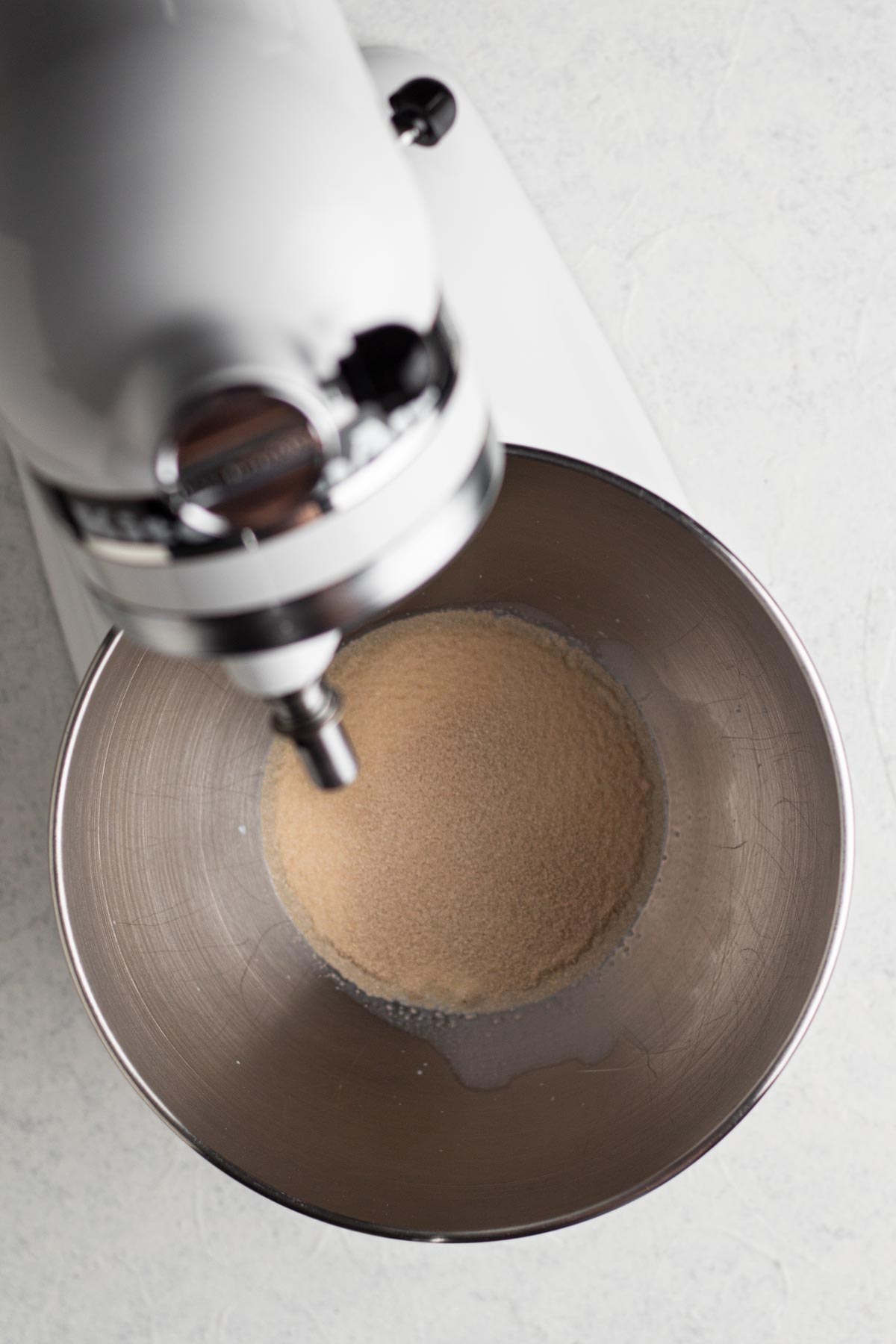 Milk and yeast in the bowl of a white stand mixer on a white surface.