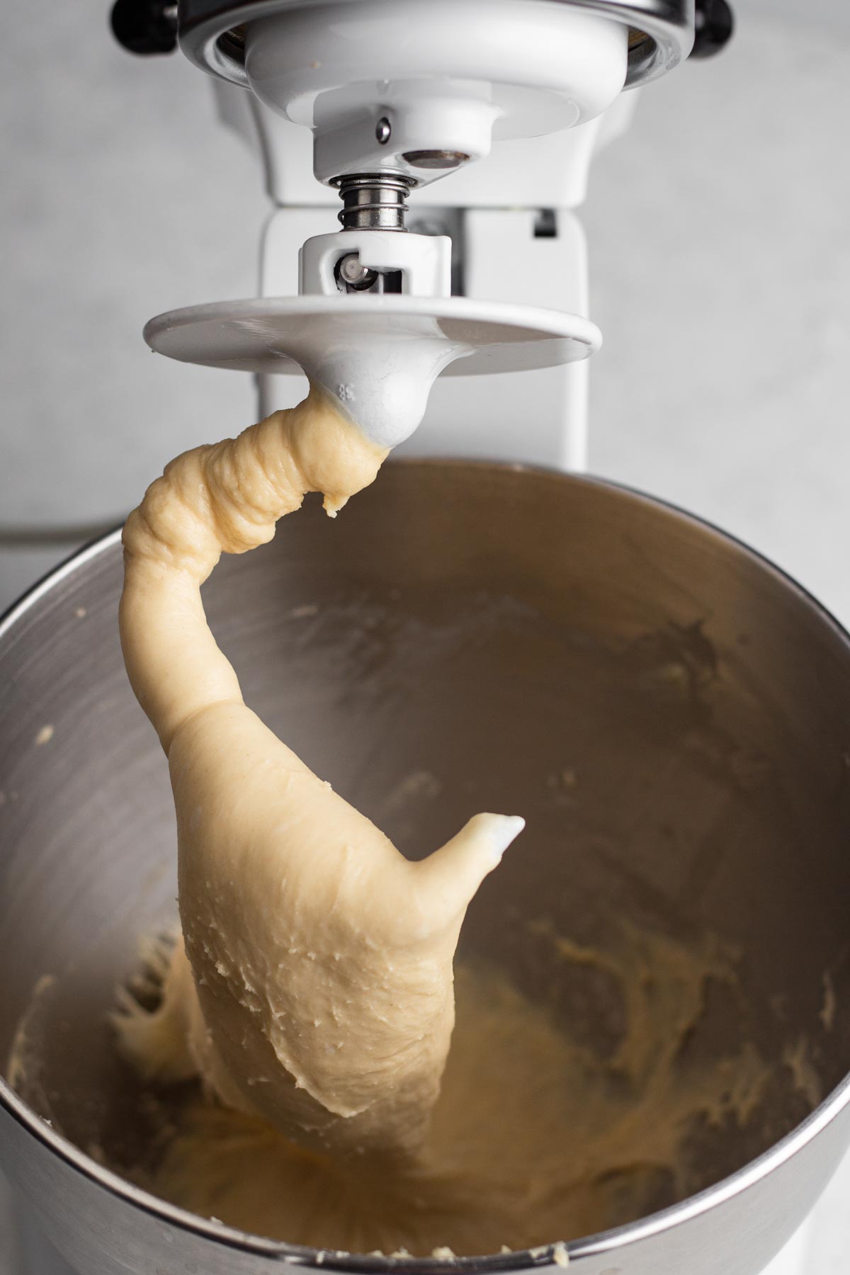 Angled view of brioche dough in the bowl of a stand mixer with a dough hook.