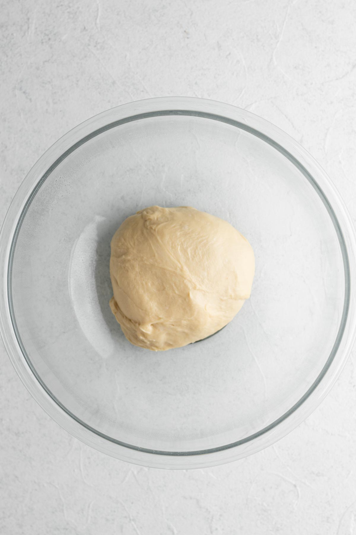 Ball of brioche dough in a glass mixing ball on a white surface.