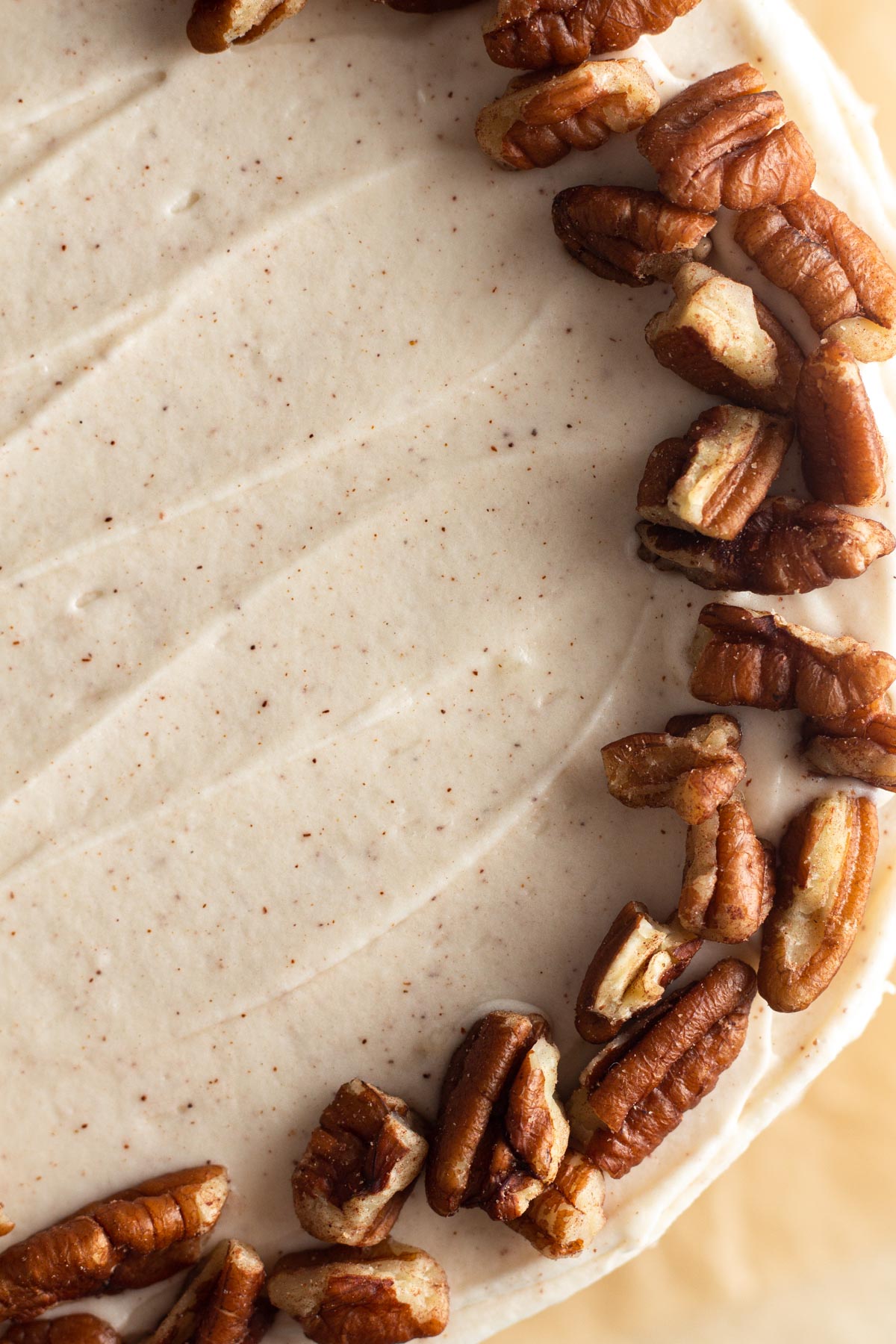 Close up overhead view of speckled frosting and chopped pecans on top of a cake.