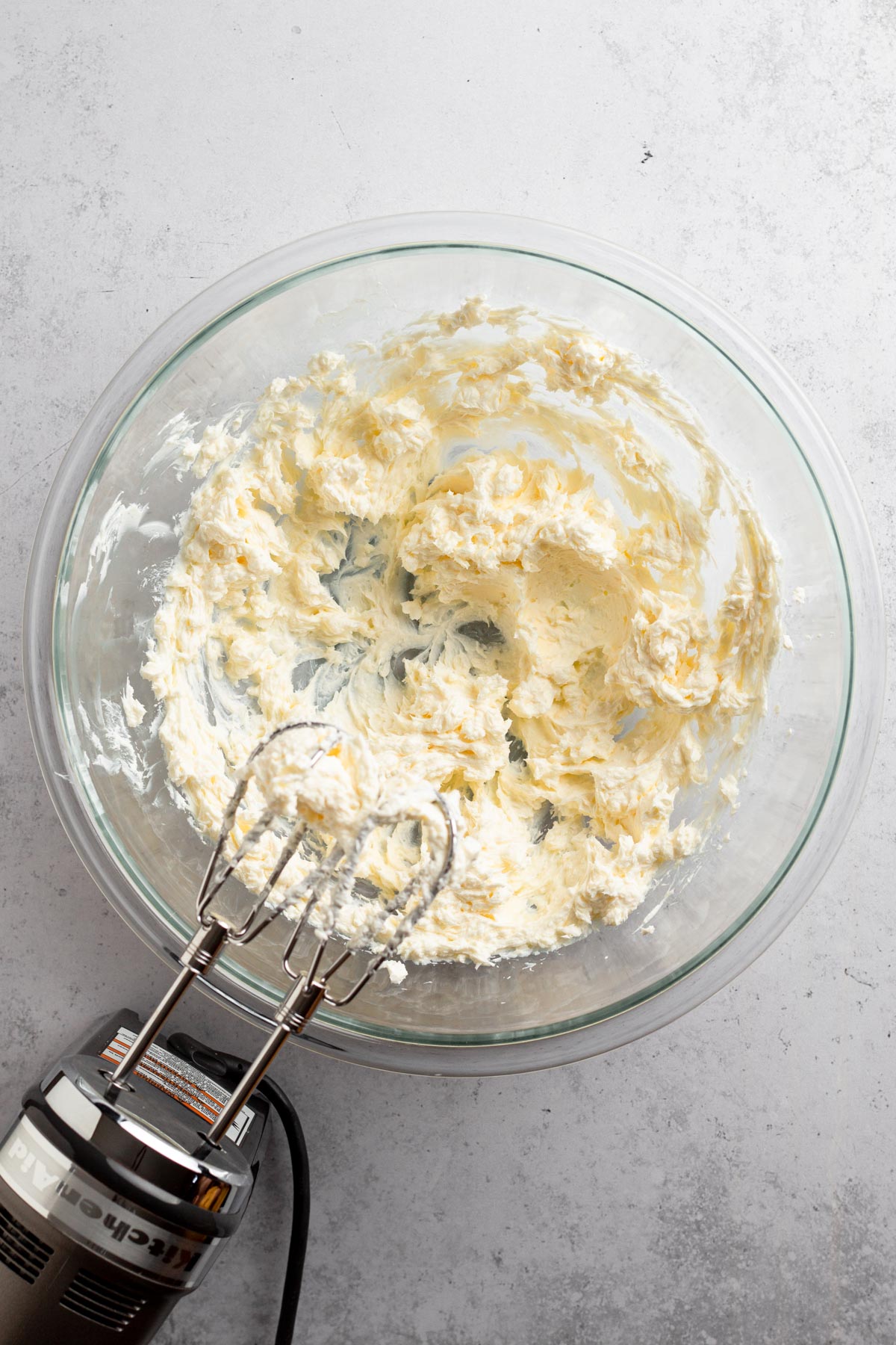 Butter and cream cheese beaten together in a glass mixing bowl on a gray surface.