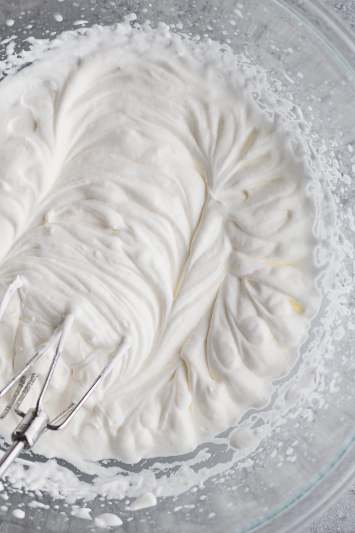 Swirls of whipped cream in a glass bowl on a gray surface.