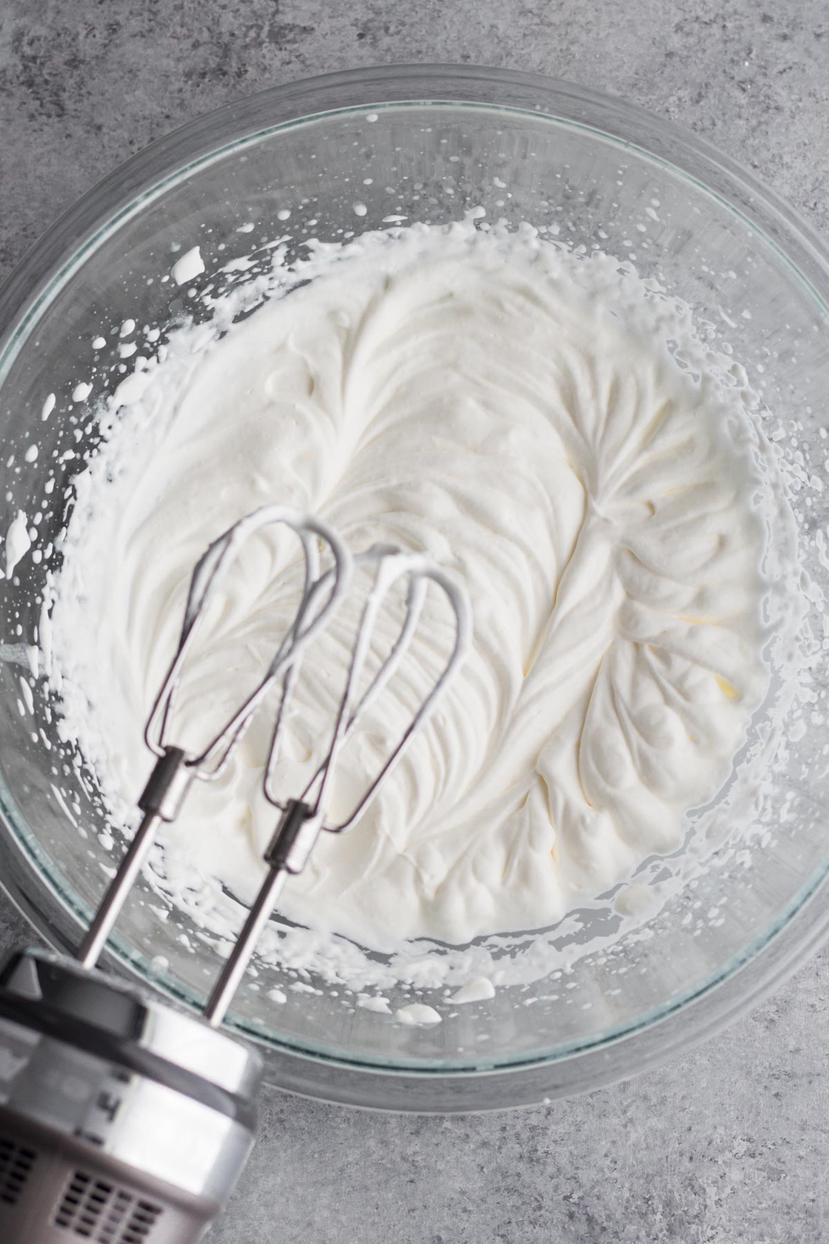 Overhead view of whipped cream in a glass bowl with an electric hand mixer.