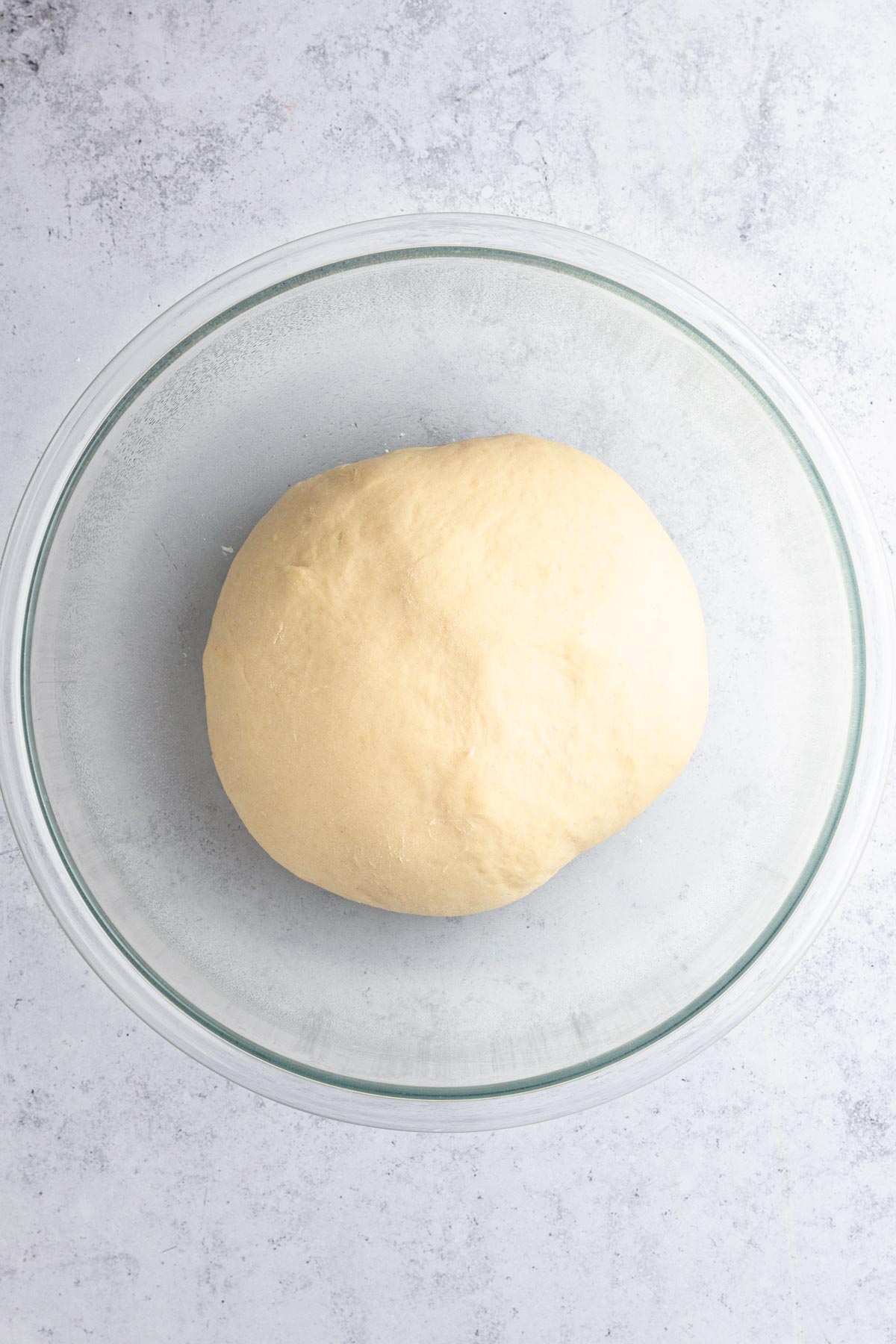 Risen ball of dough in a glass bowl on a gray surface.