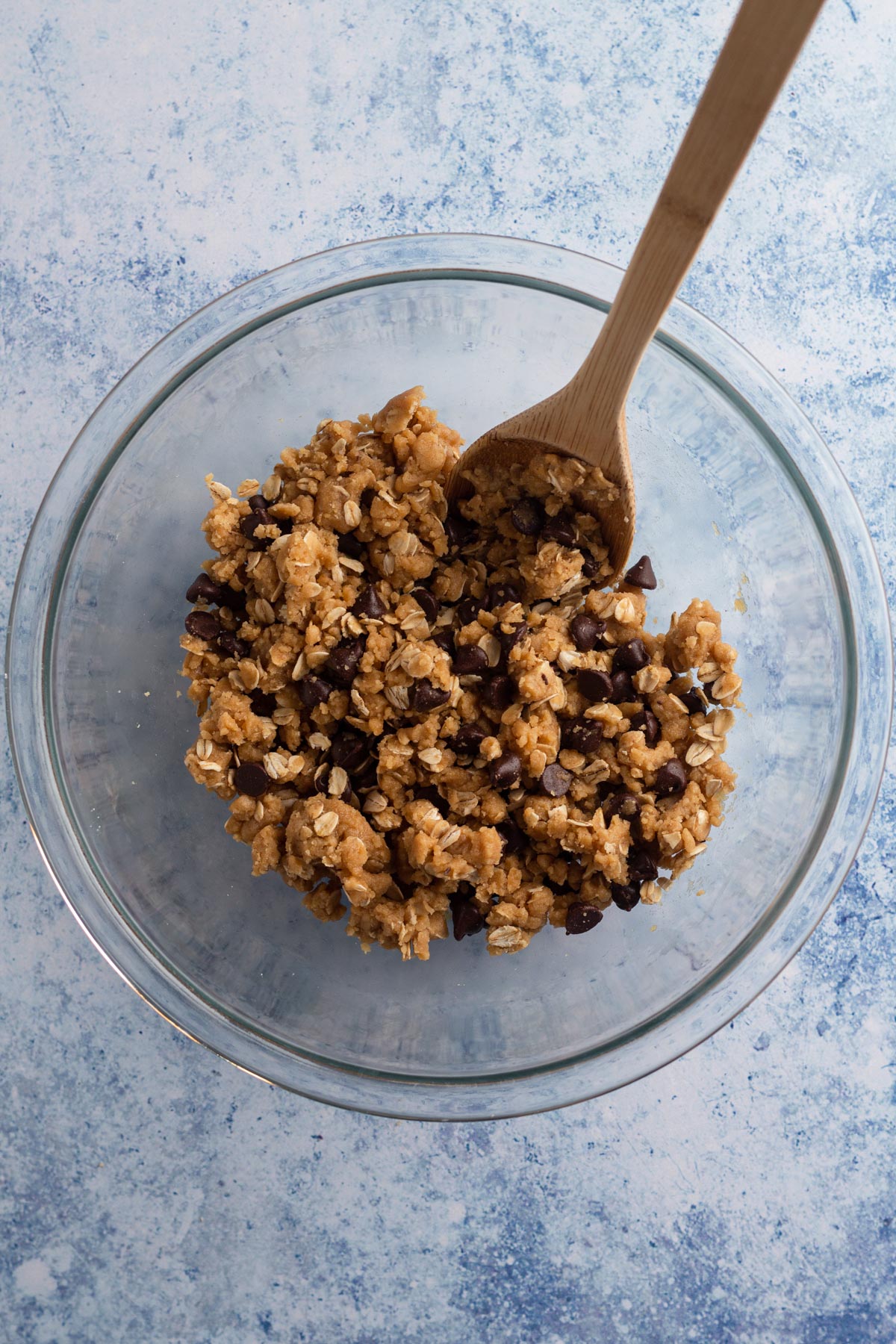 Cookie dough in a glass bowl with a wooden spoon on a blue background.
